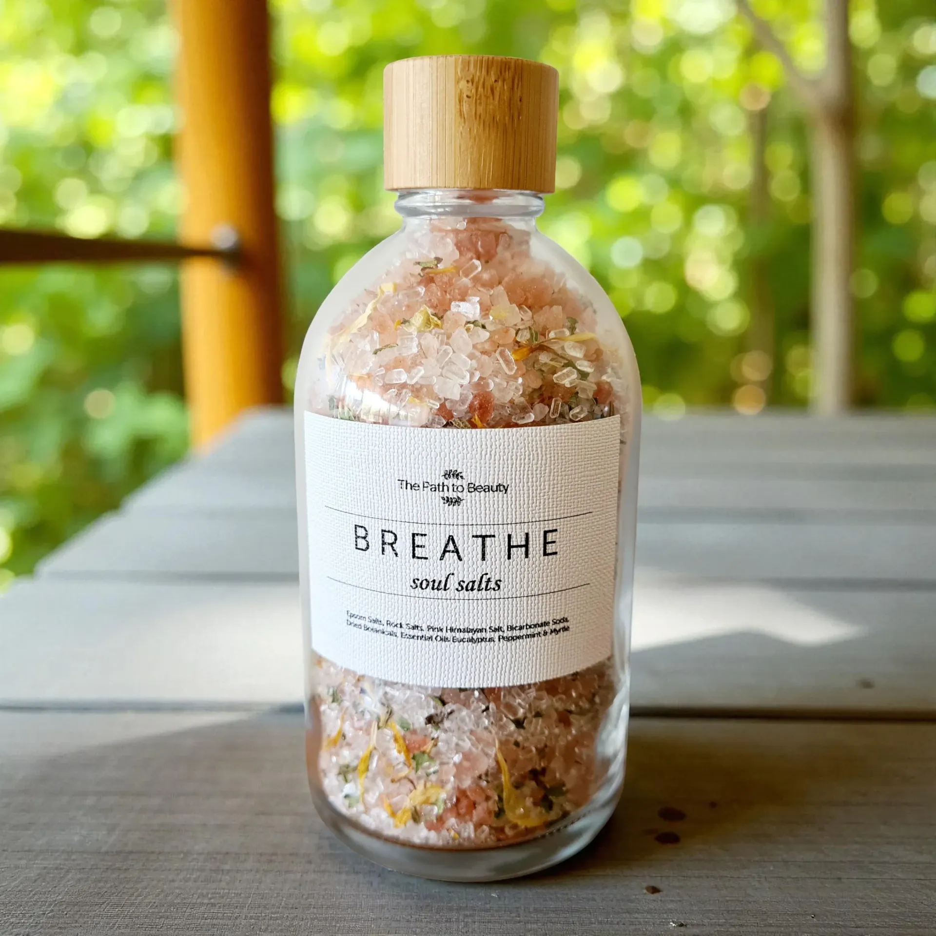 Glass jar of pink bath salts labeled “BREATHE” with a wooden lid on an outdoor table