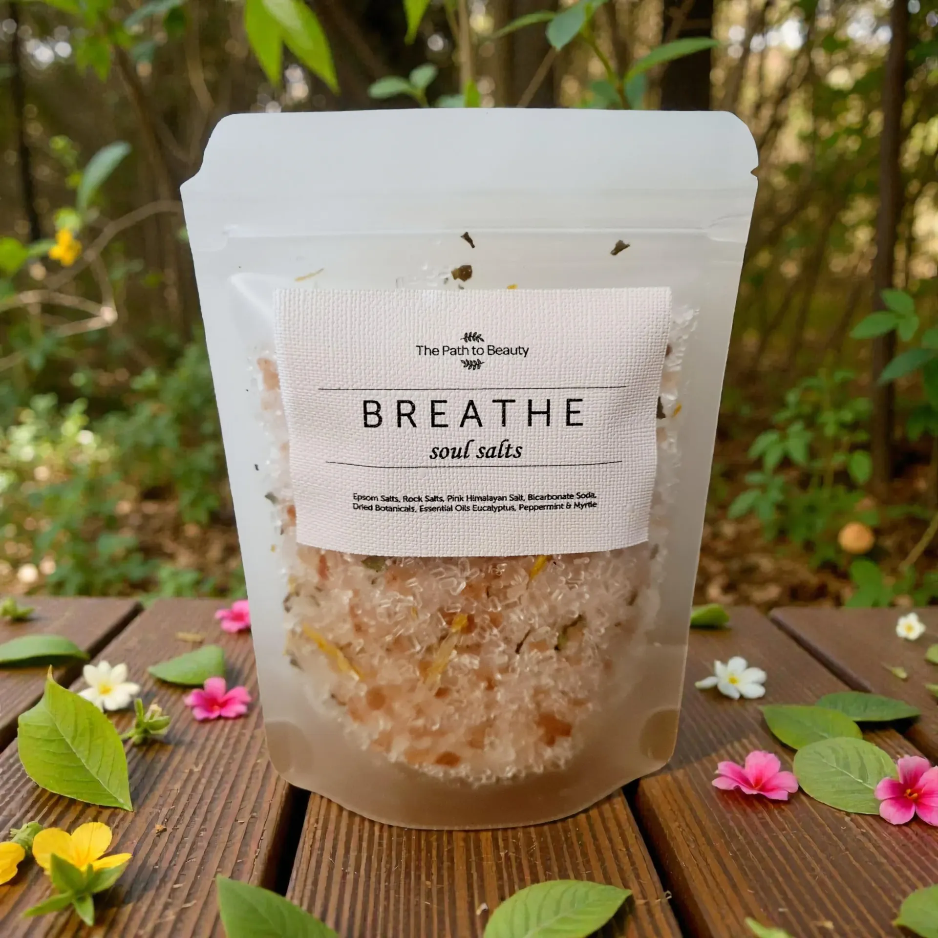 Breathe pink bath salt pouch on a wooden table with flowers and greenery outdoors