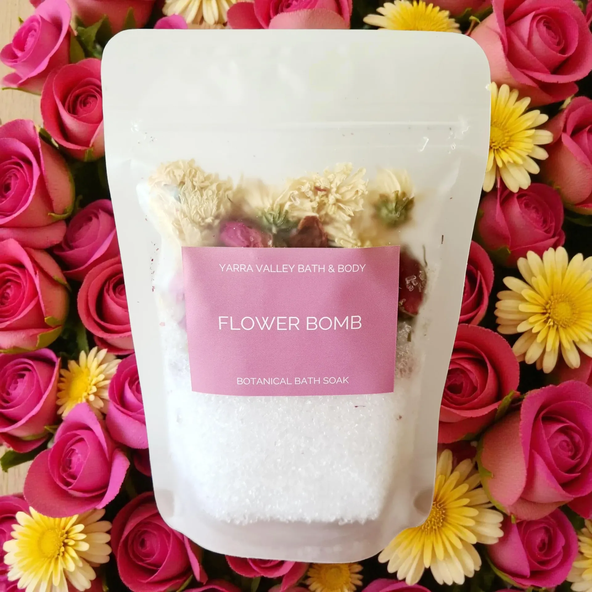 White pouch labeled “Flower Bomb” bath soak against a pink-and-yellow flower background
