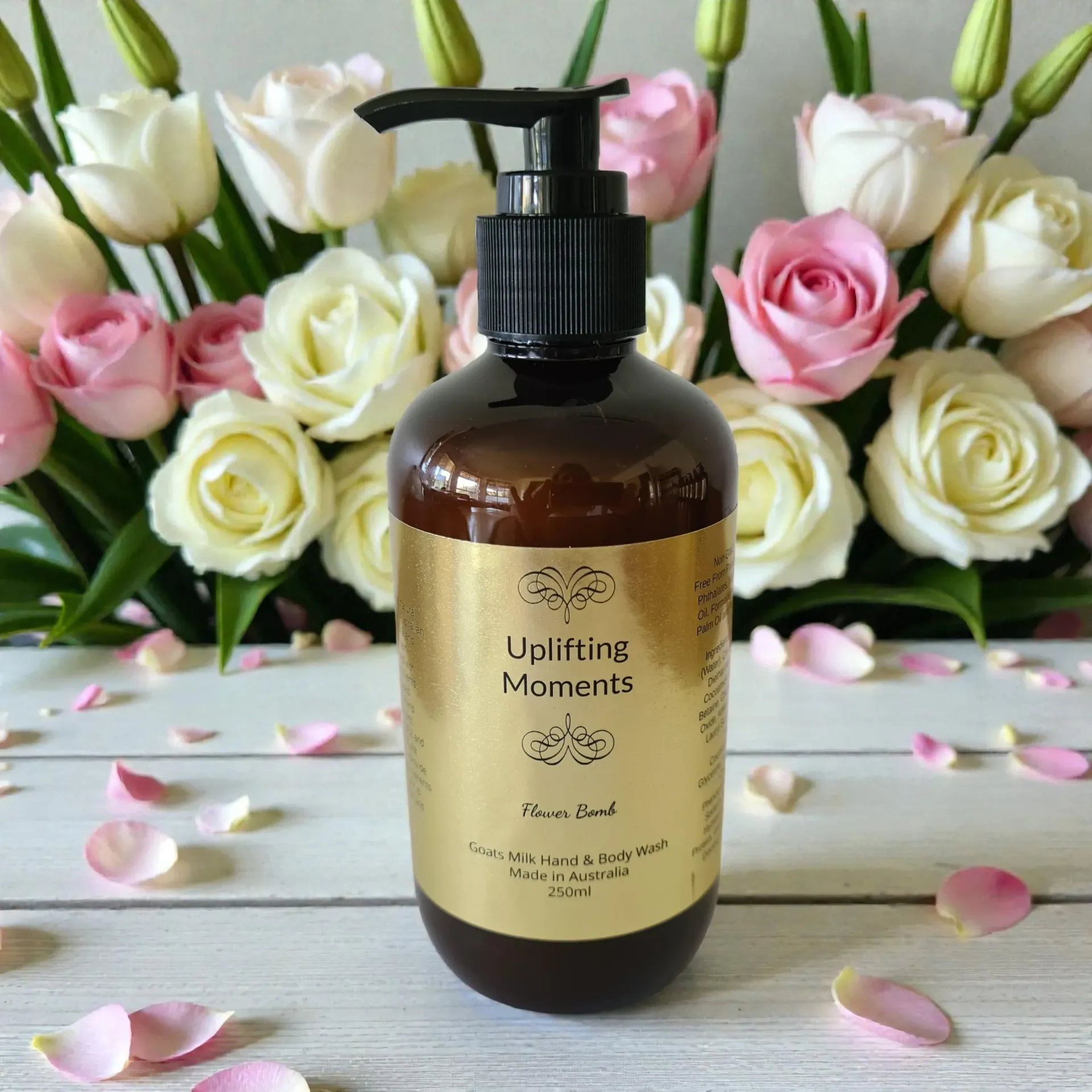 Amber pump bottle of Uplifting Moments Flower Bomb hand and body wash with pink and white roses in the background