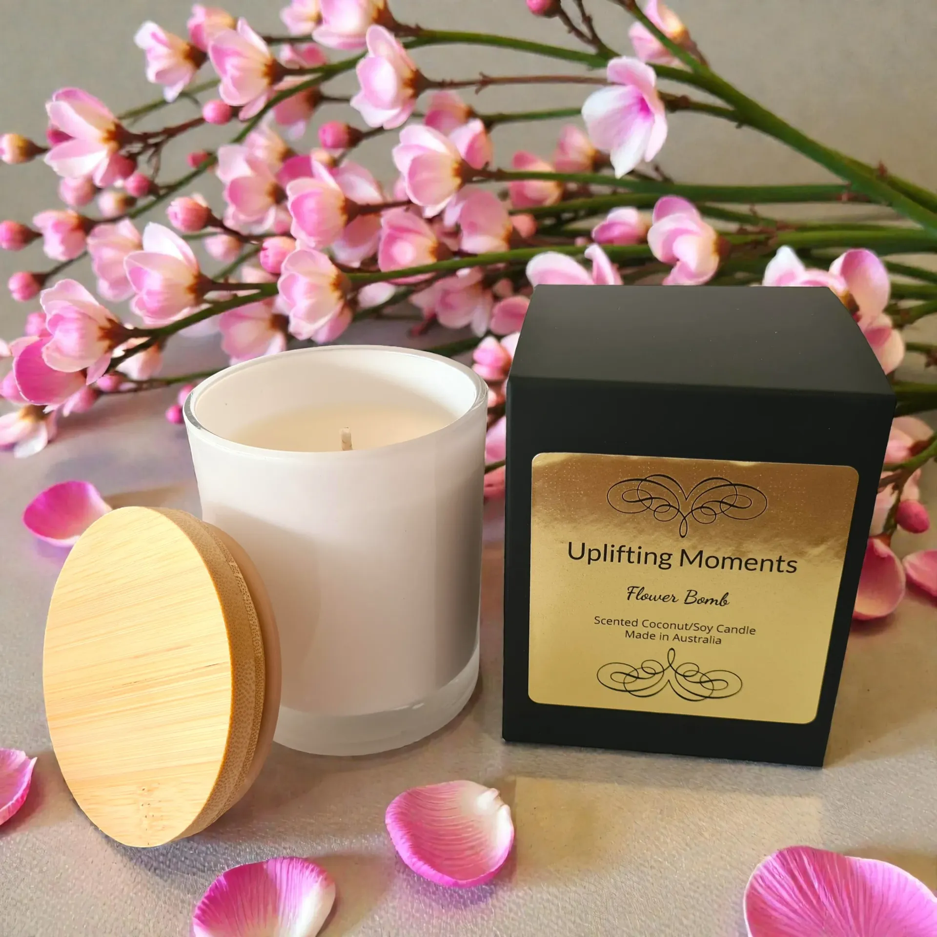 White candle with a round wooden lid, surrounded by pink and cream flowers on a soft background