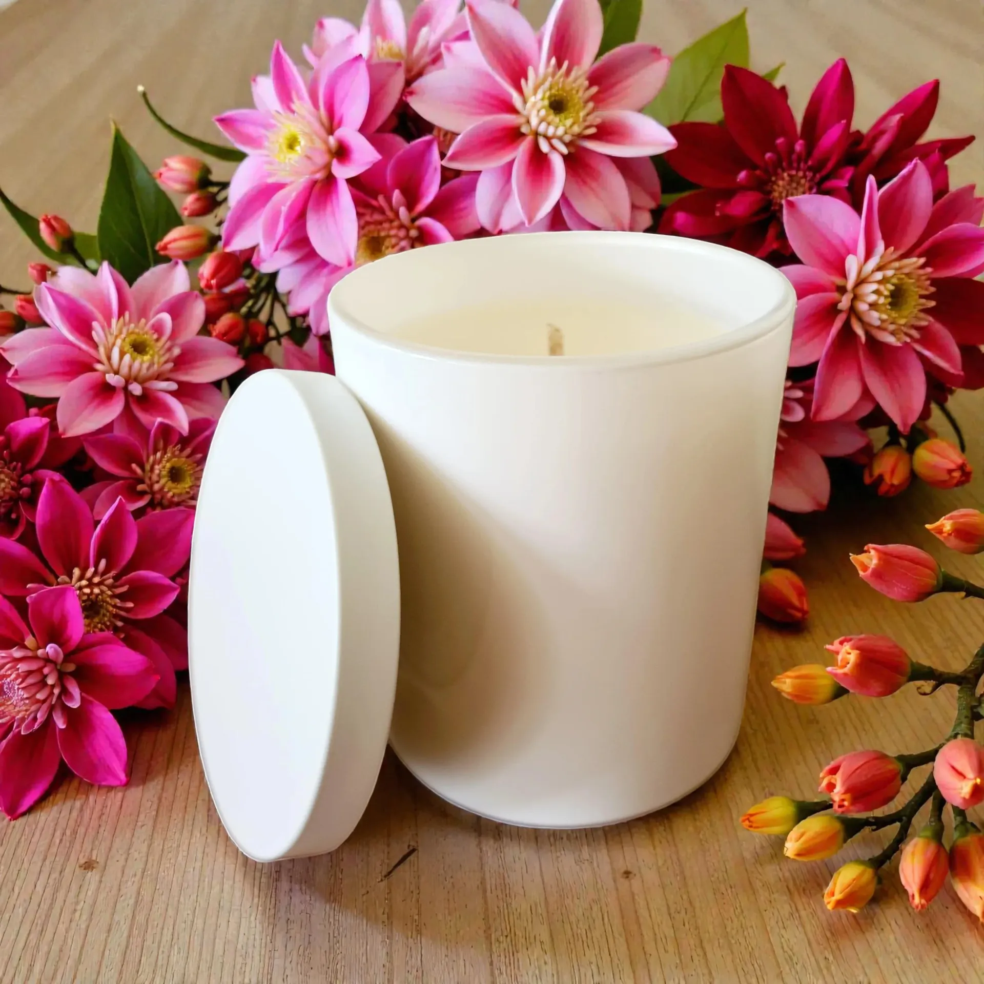 White candle with lid surrounded by pink and red flowers on a wooden surface