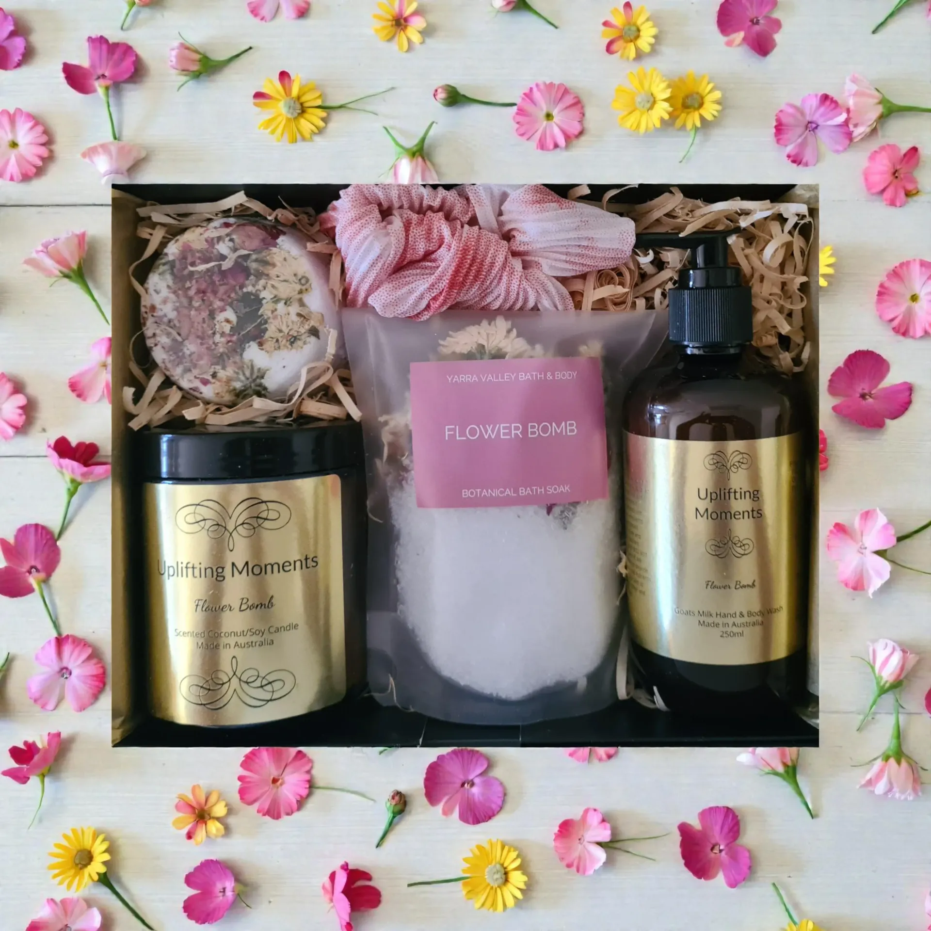 Gift box with pink flowers, a bath bomb, candle jar, and two amber bottles on a white floral background