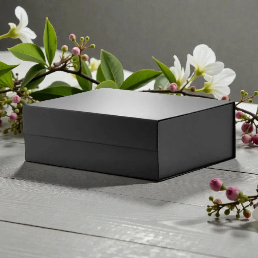 Black rectangular gift box on a gray wooden surface with white and pink flowers nearby