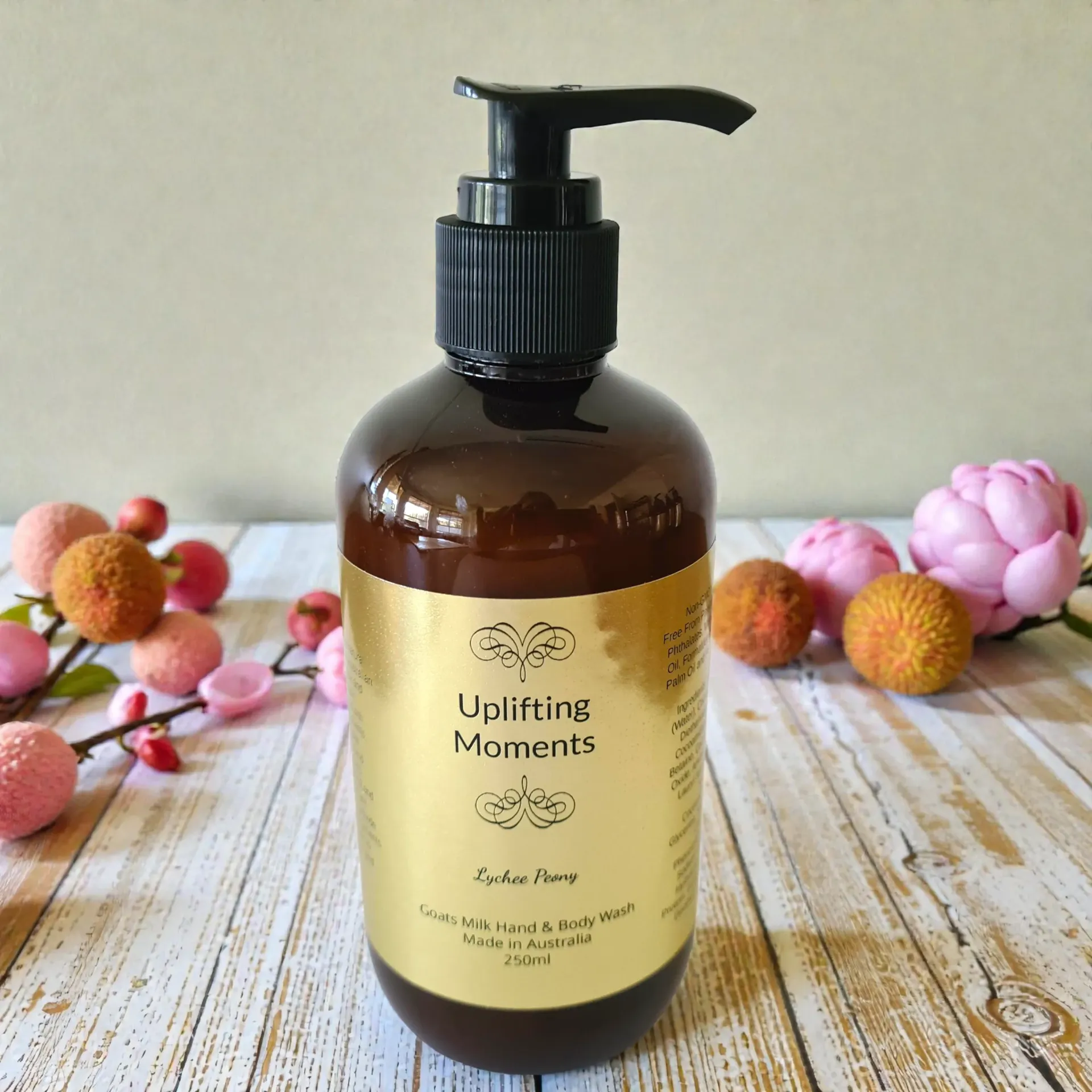 Amber pump bottle of Uplifting Moments Flower Bomb hand and body wash with pink and white roses in the background
