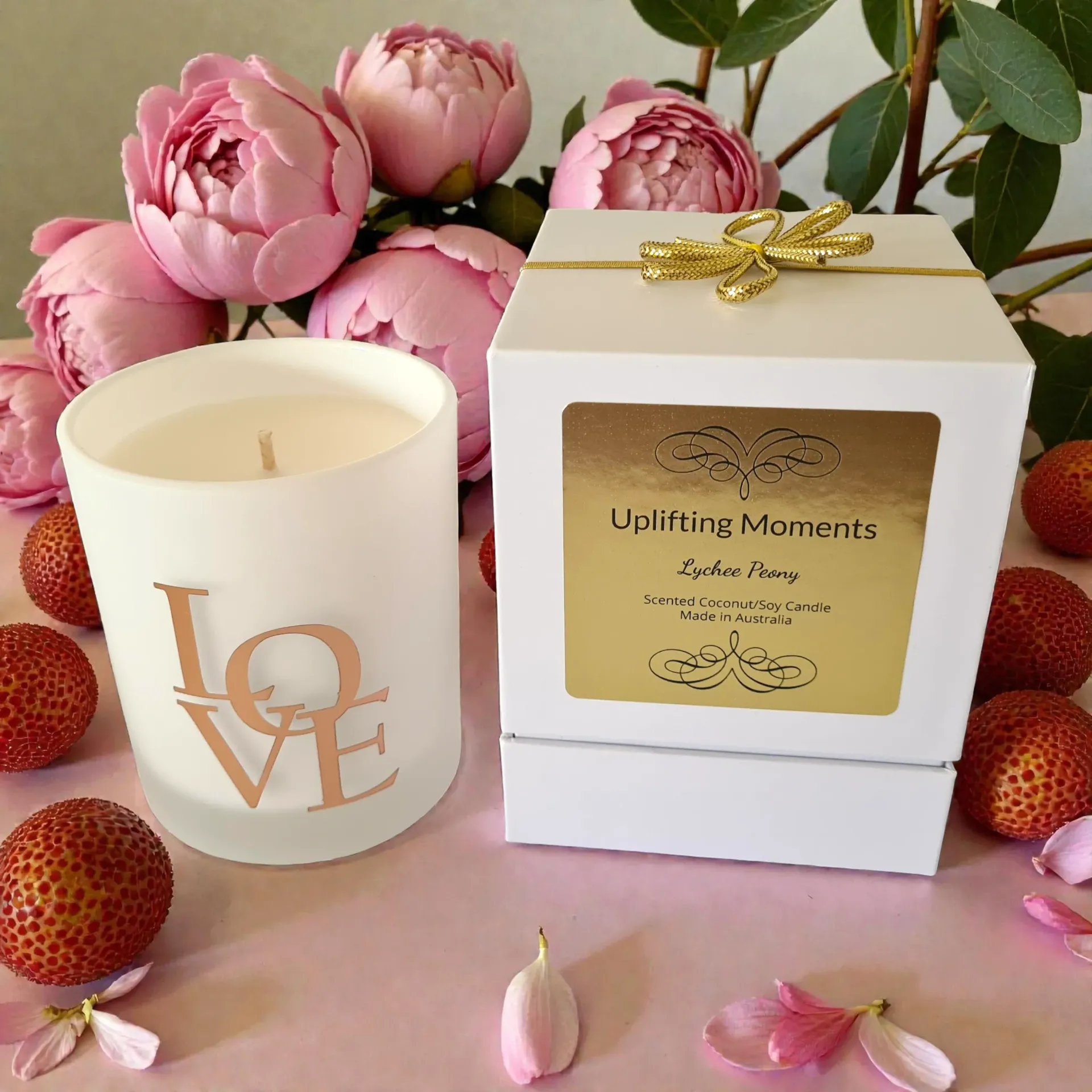 White candle with rose gold “LOVE” text surrounded by pink flowers and red berries