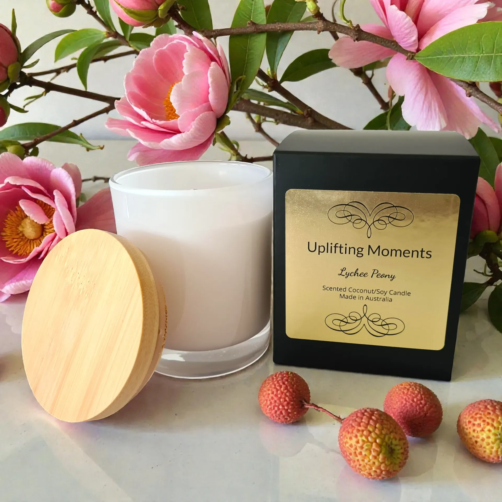 White candle with pink flower, round wooden lid, and berry-like fruits on a wooden surface