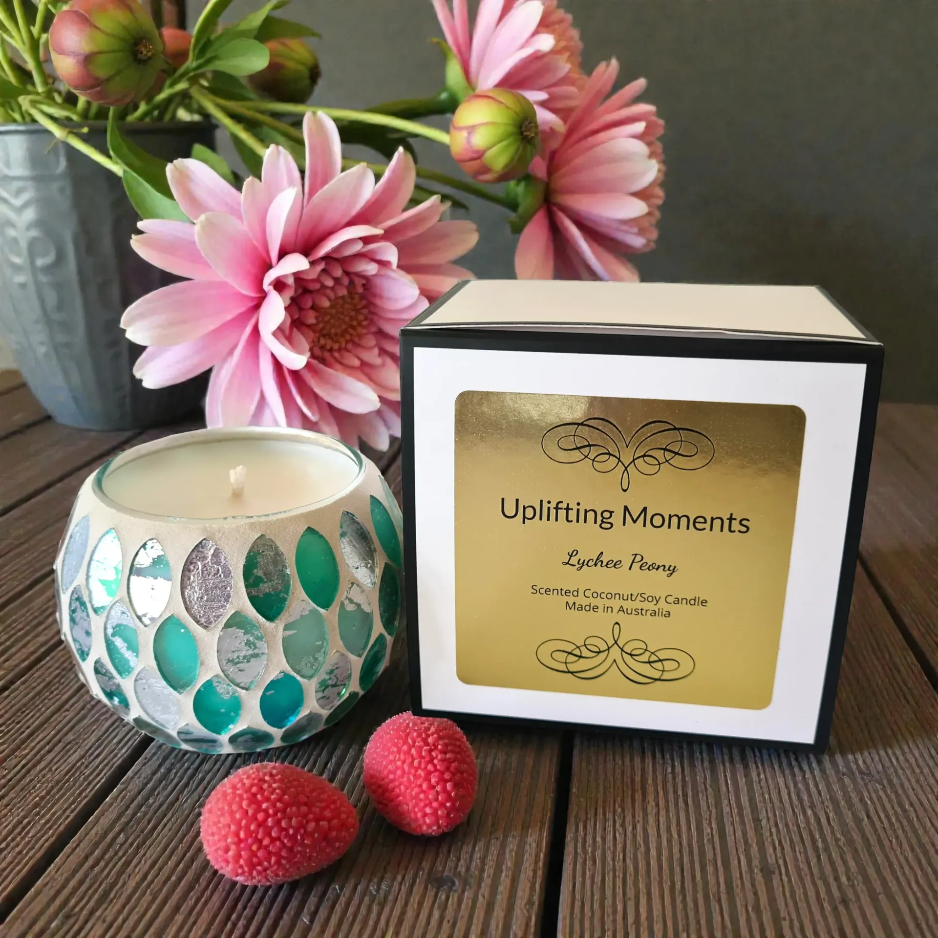 White candle in a turquoise mosaic holder on a wooden slice, with pink flowers in the background