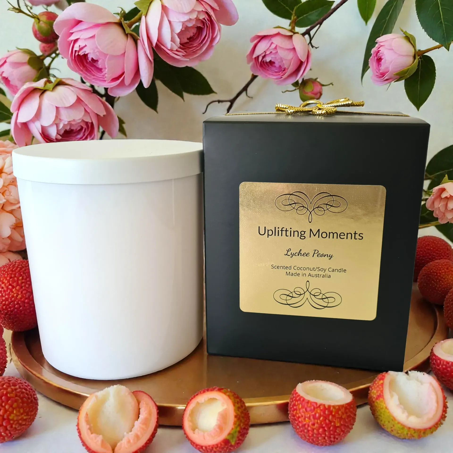 White candle jar with lid beside pink flowers and fruit on a wooden table