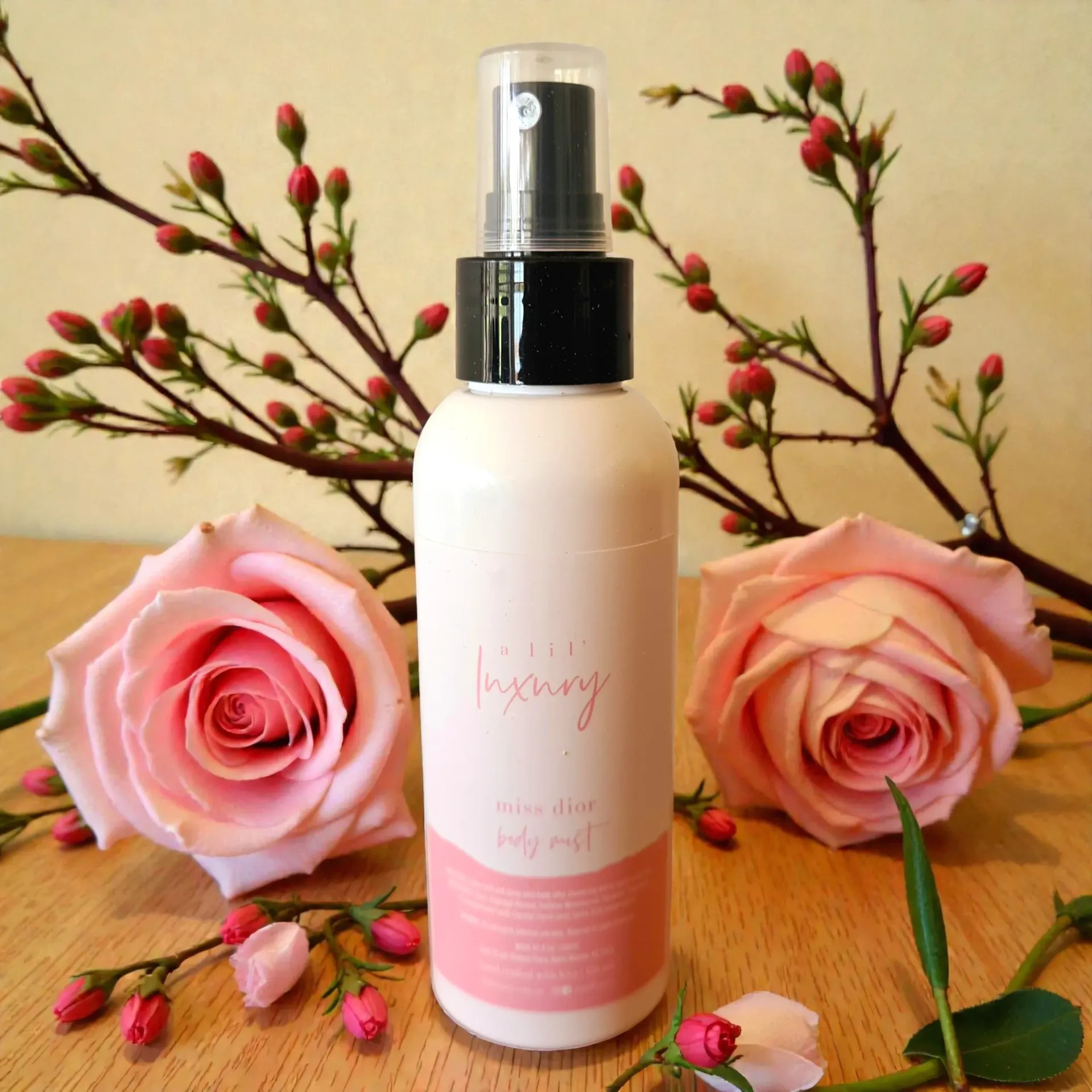 Pink body mist spray bottle between two pink roses on a beige background
