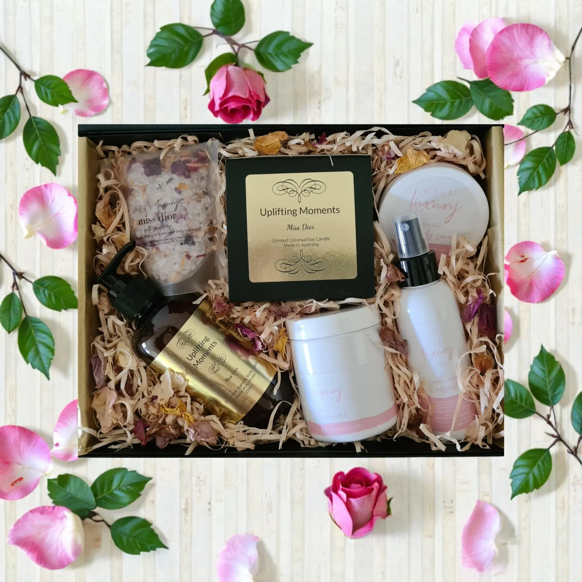 Gift box of Miss Dior type scented bath and body products and candle with pink roses on a white wood background