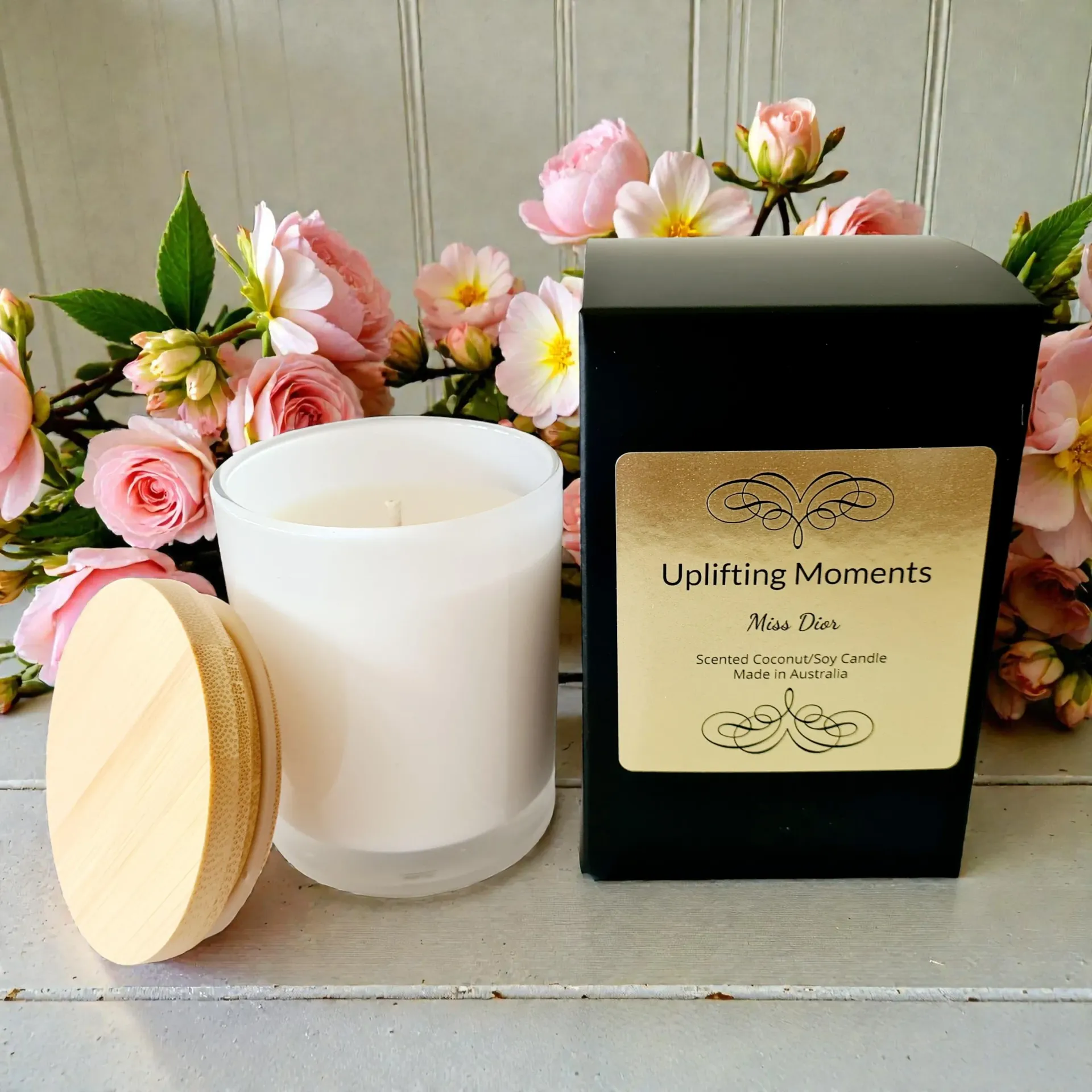 White candle with lid, surrounded by pastel flowers on a wooden surface