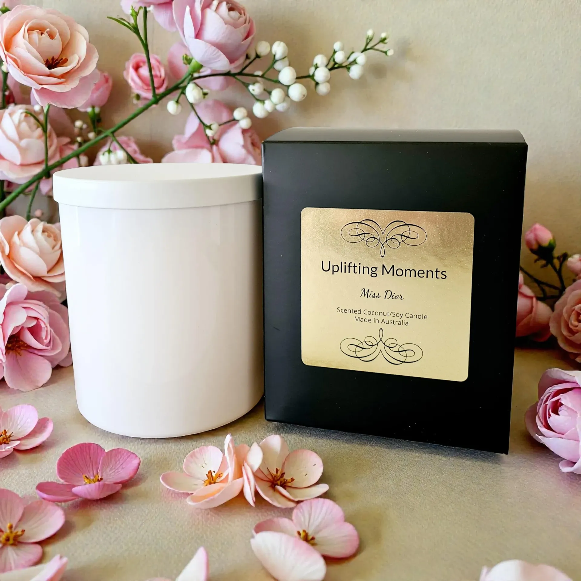 White candle jar with lid, surrounded by pink and cream flowers on a beige surface