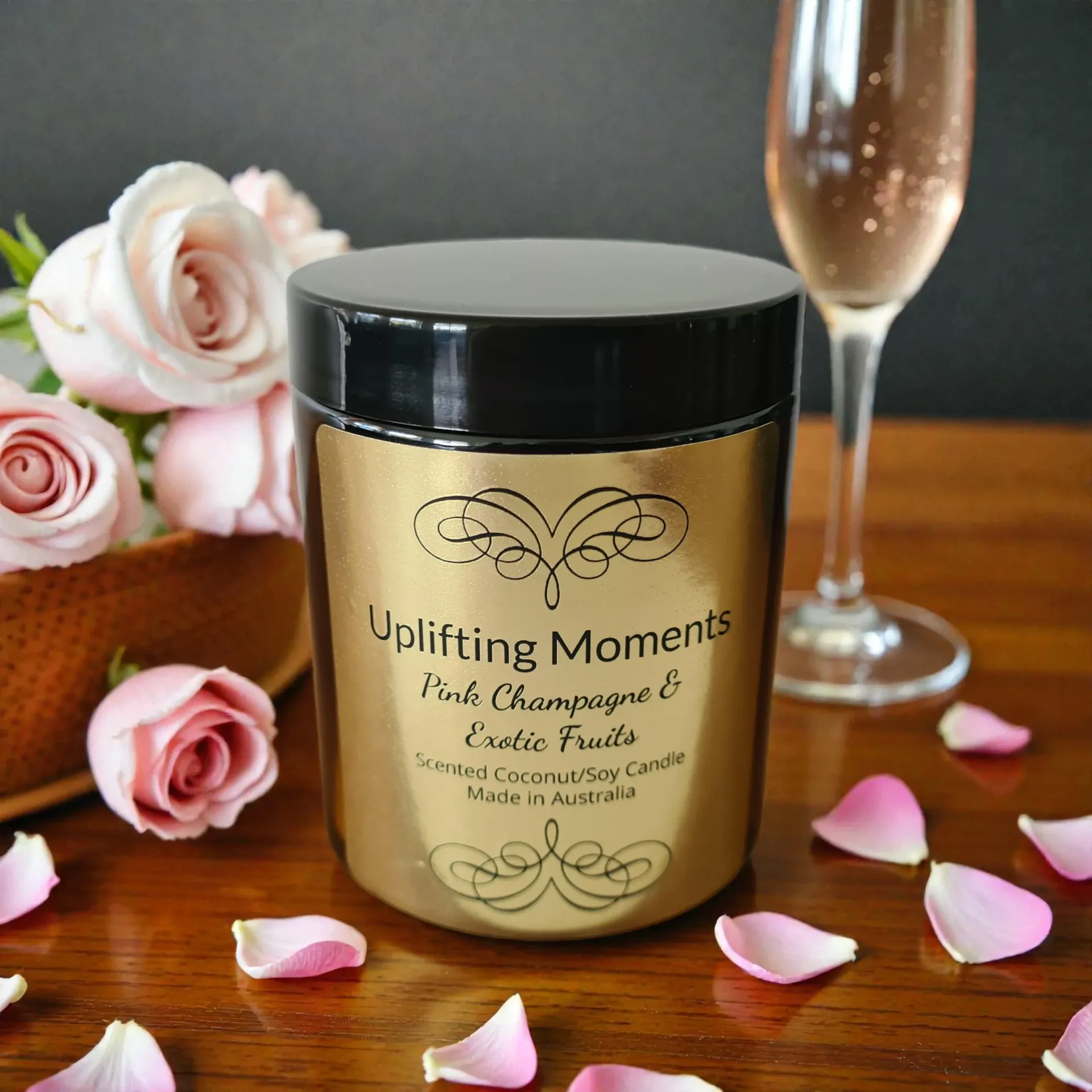 A candle jar with black lid, pink roses, scattered petals, and a champagne flute on a wooden surface.