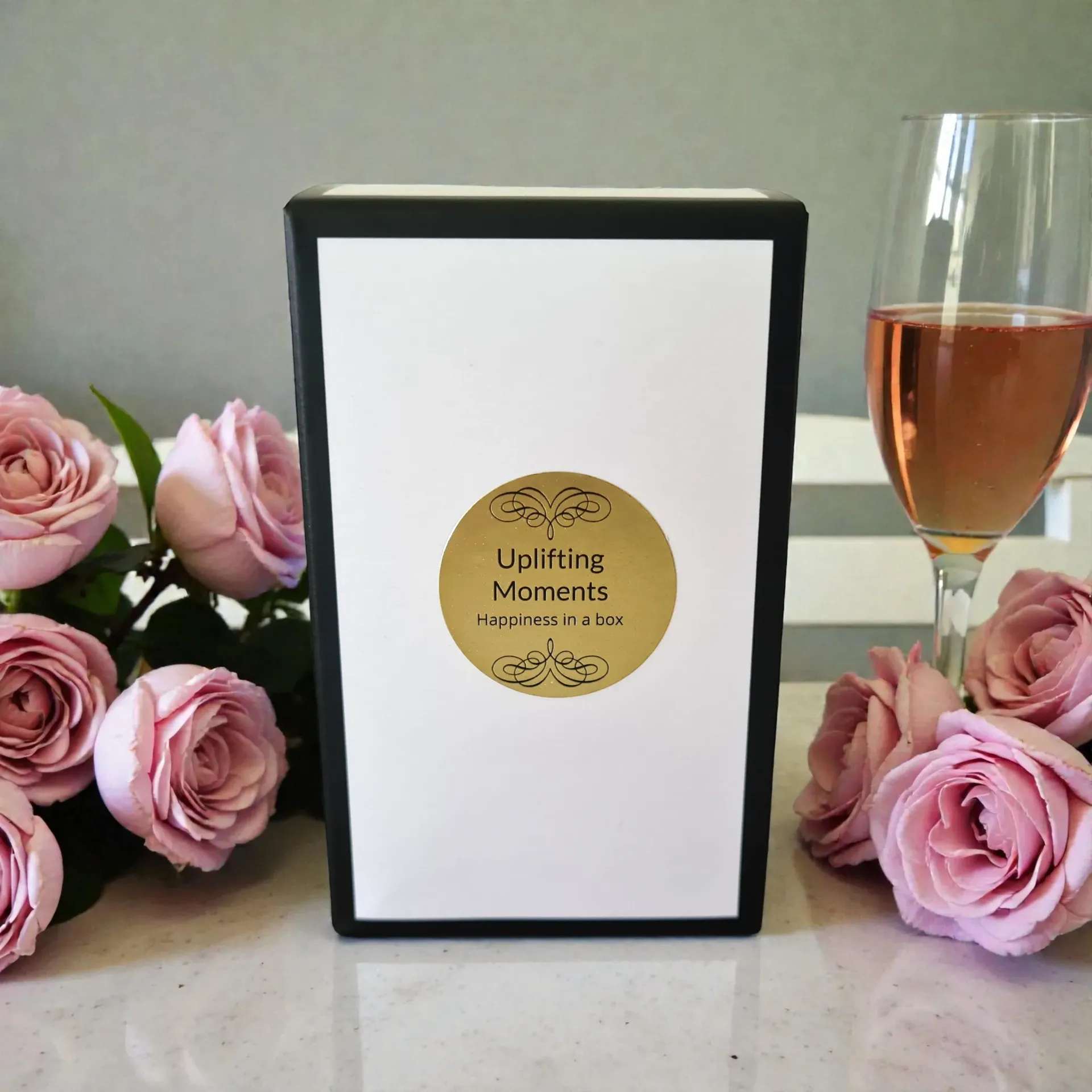 Frosted candle with “Uplifting Moments” label, pink roses, and a rosé wine glass on a soft-lit table