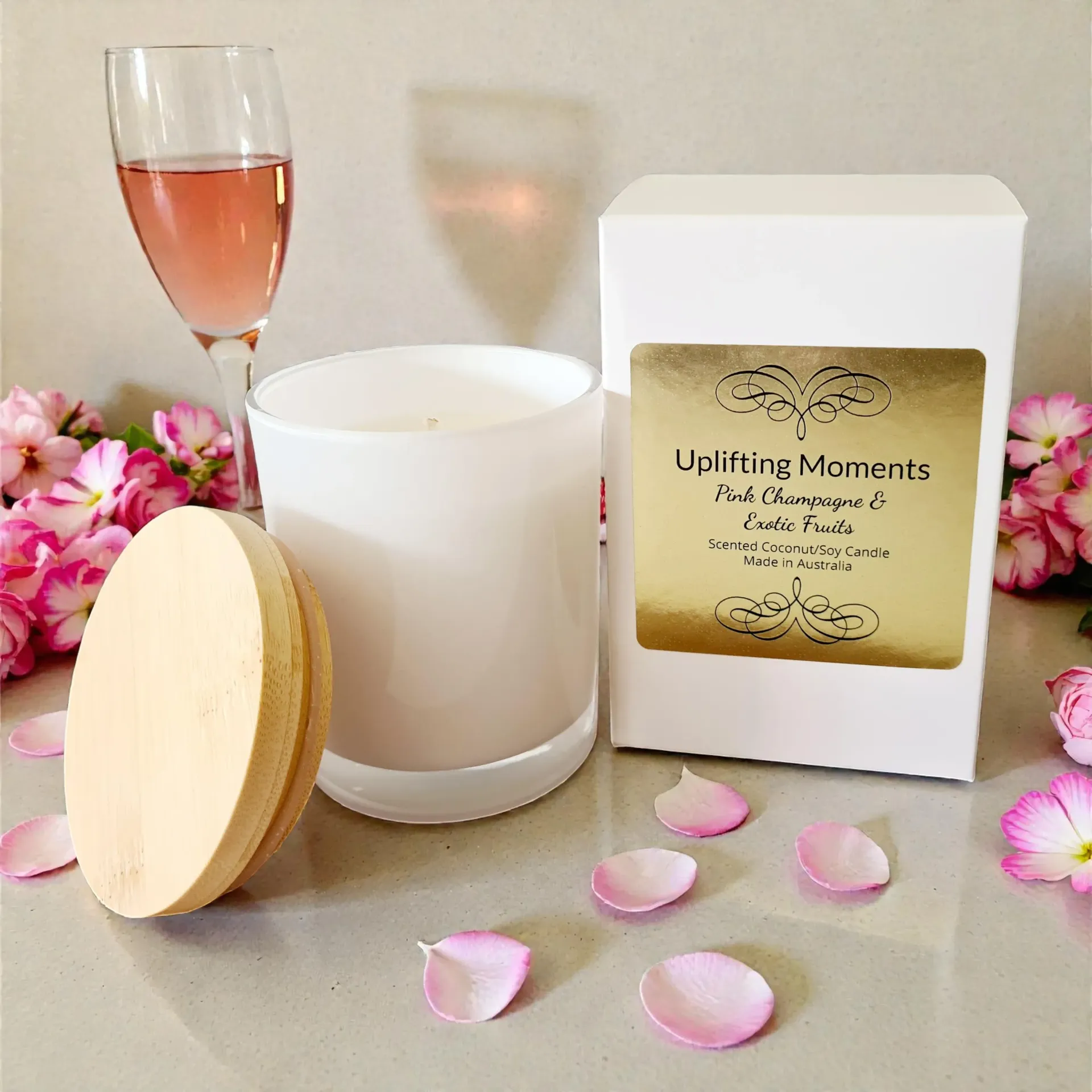 White candle with wooden lid, wine glass, and pink flowers on a soft beige surface
