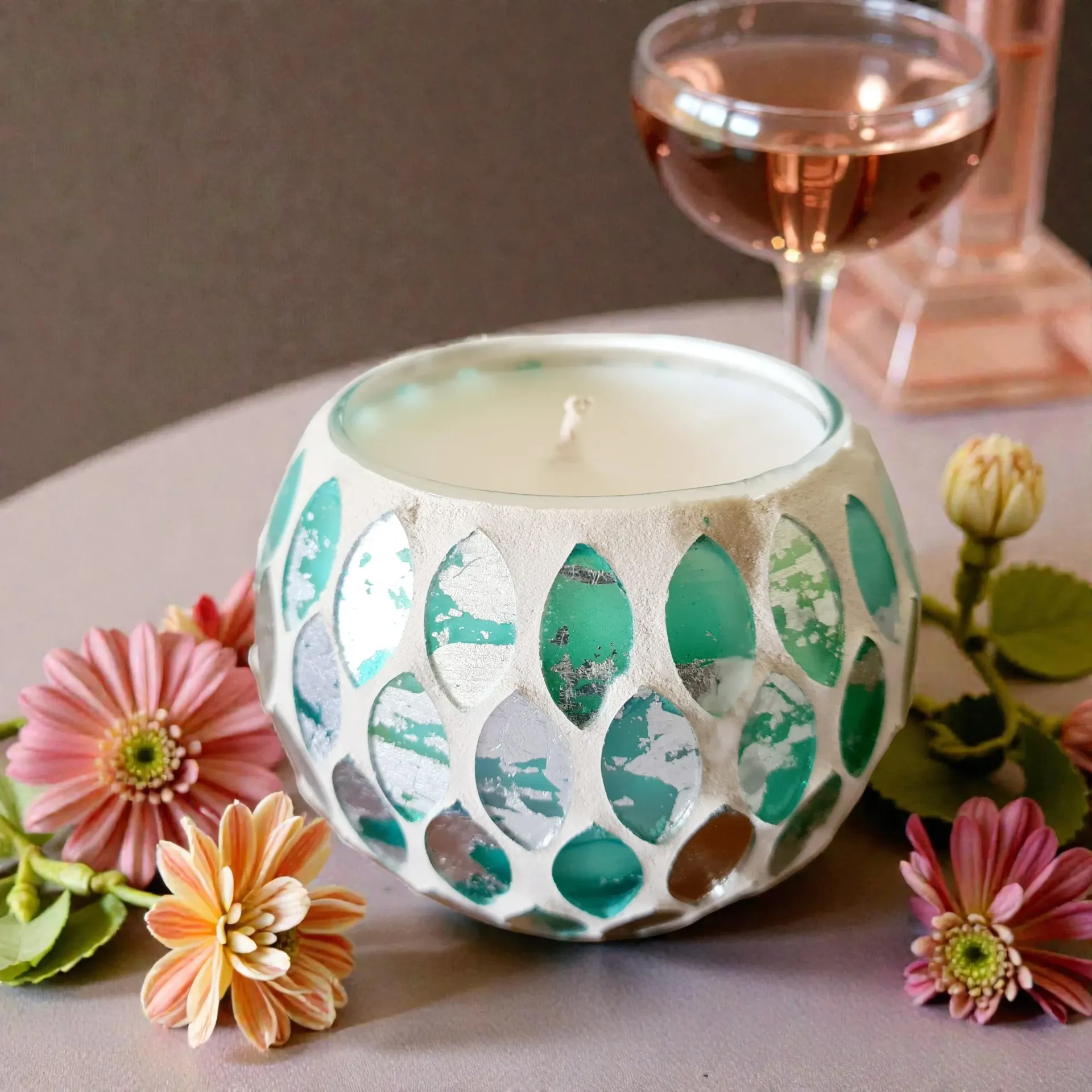 Decorative white-and-teal candle holder with flowers beside a wine glass on a table