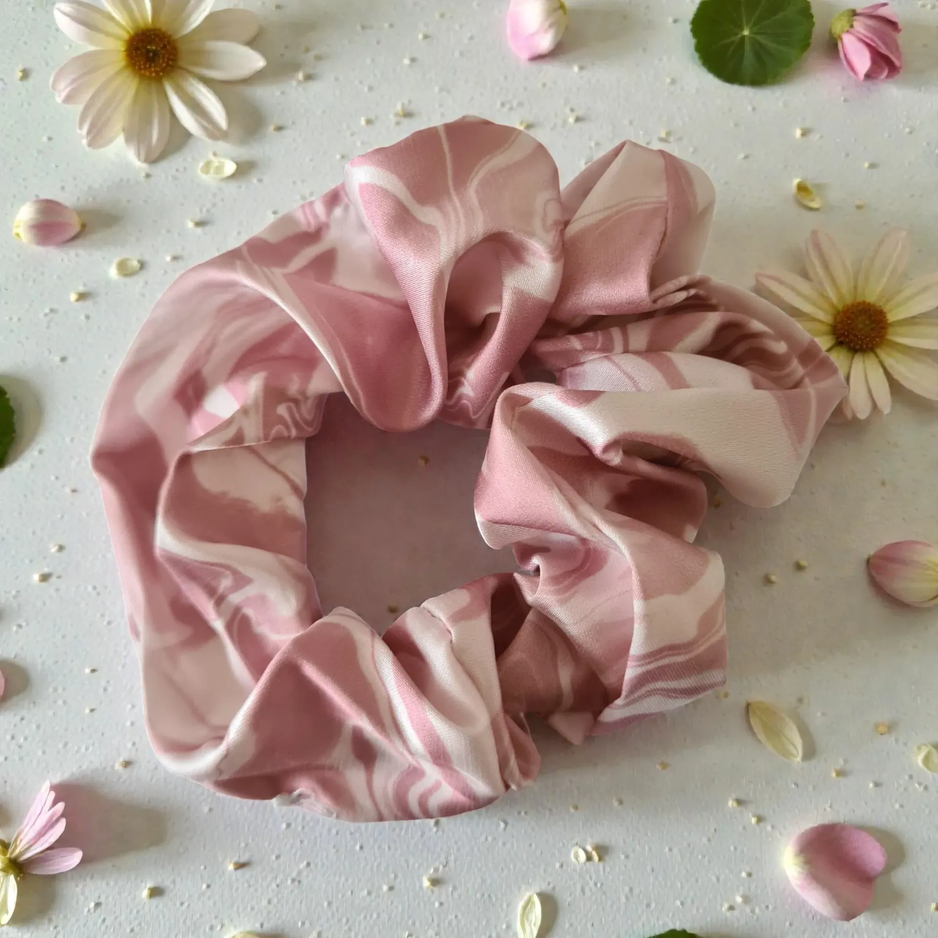 Pink satin scrunchie with white zebra stripes on a light floral background with scattered petals
