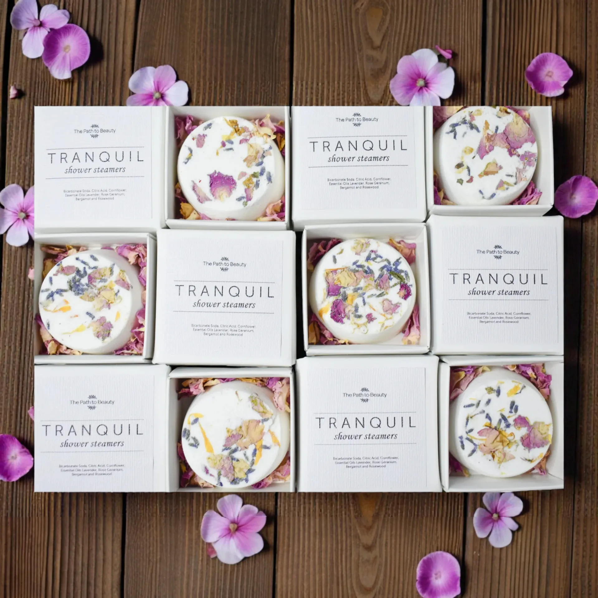 Tranquil shower steamers in white boxes with floral prints, arranged on a wooden surface with purple petals