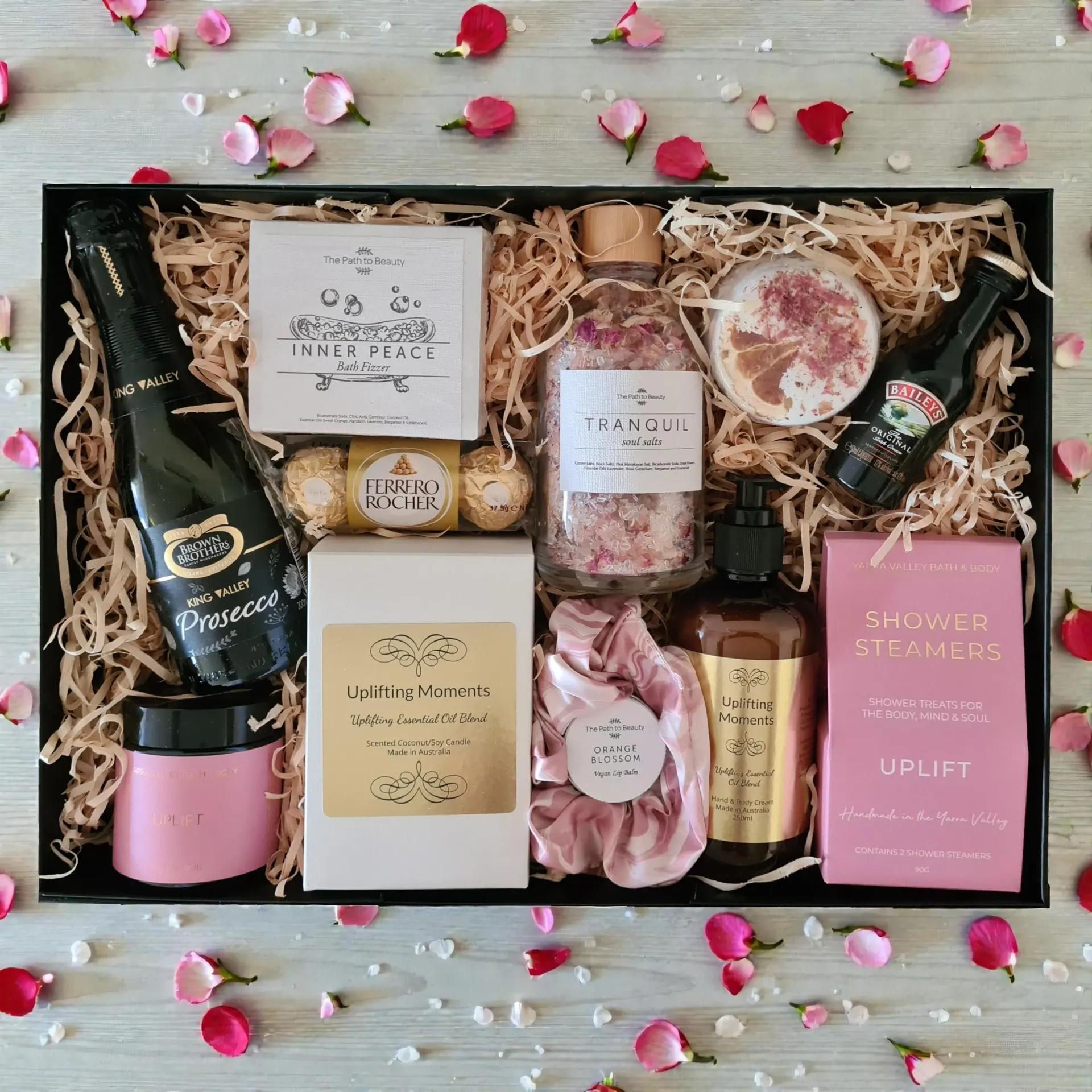 Gift box with assorted pink and gold bath, beauty, and self-care items on a wooden background