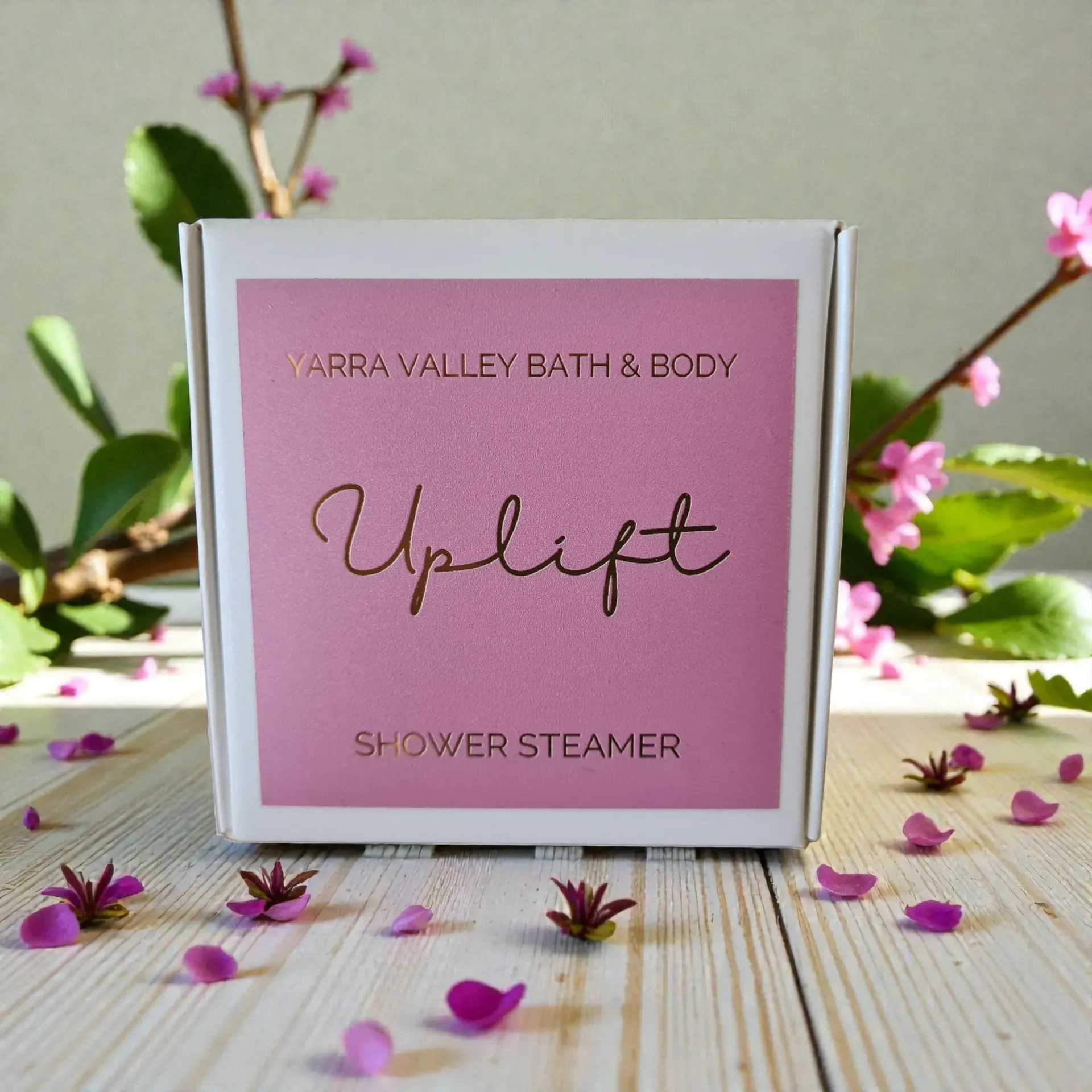 Pink Yarra Valley Bath & Body “Uplift” shower steamer box with flower petals on a wooden surface
