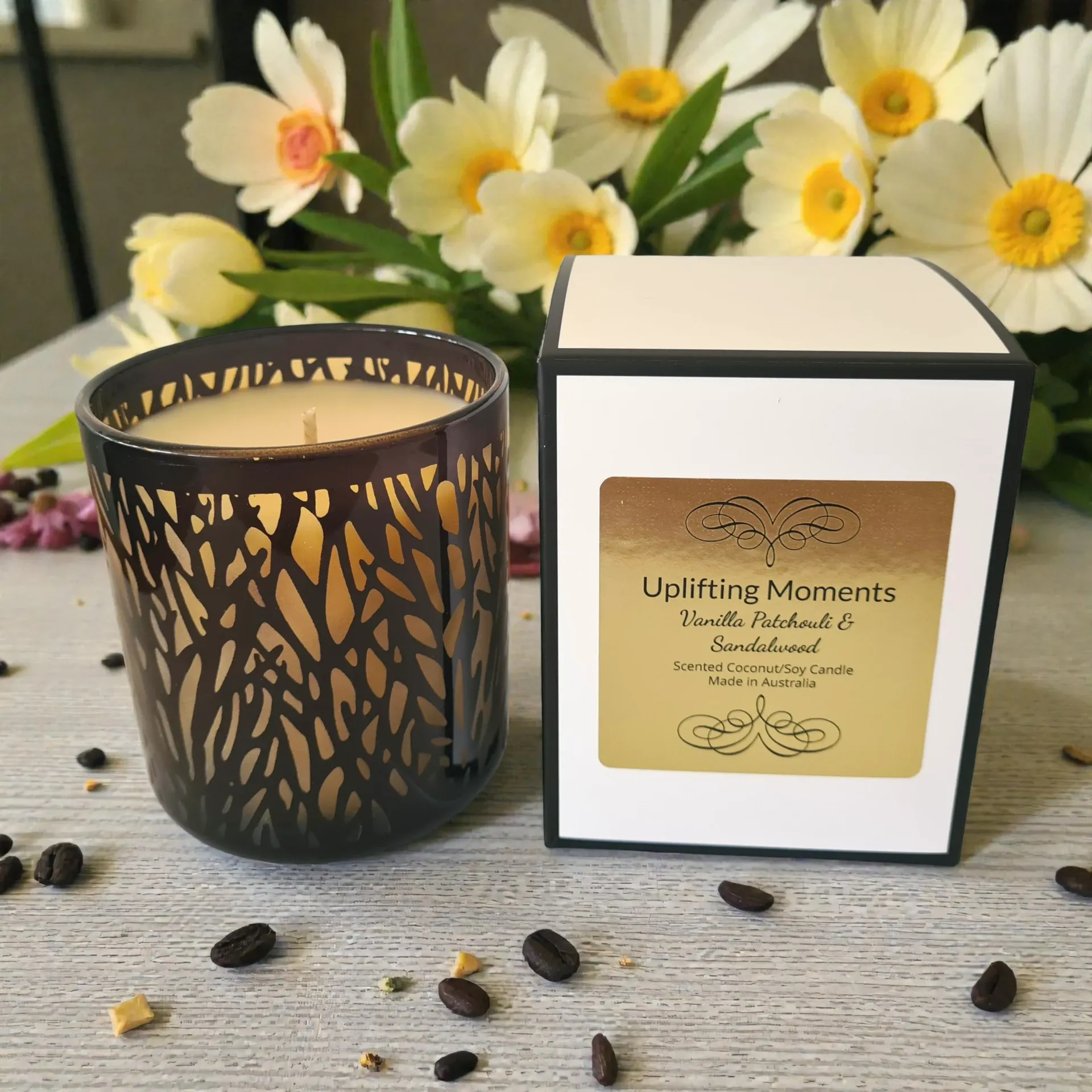 Decorative dark glass candle holder on a wooden table with white flowers and scattered pebbles