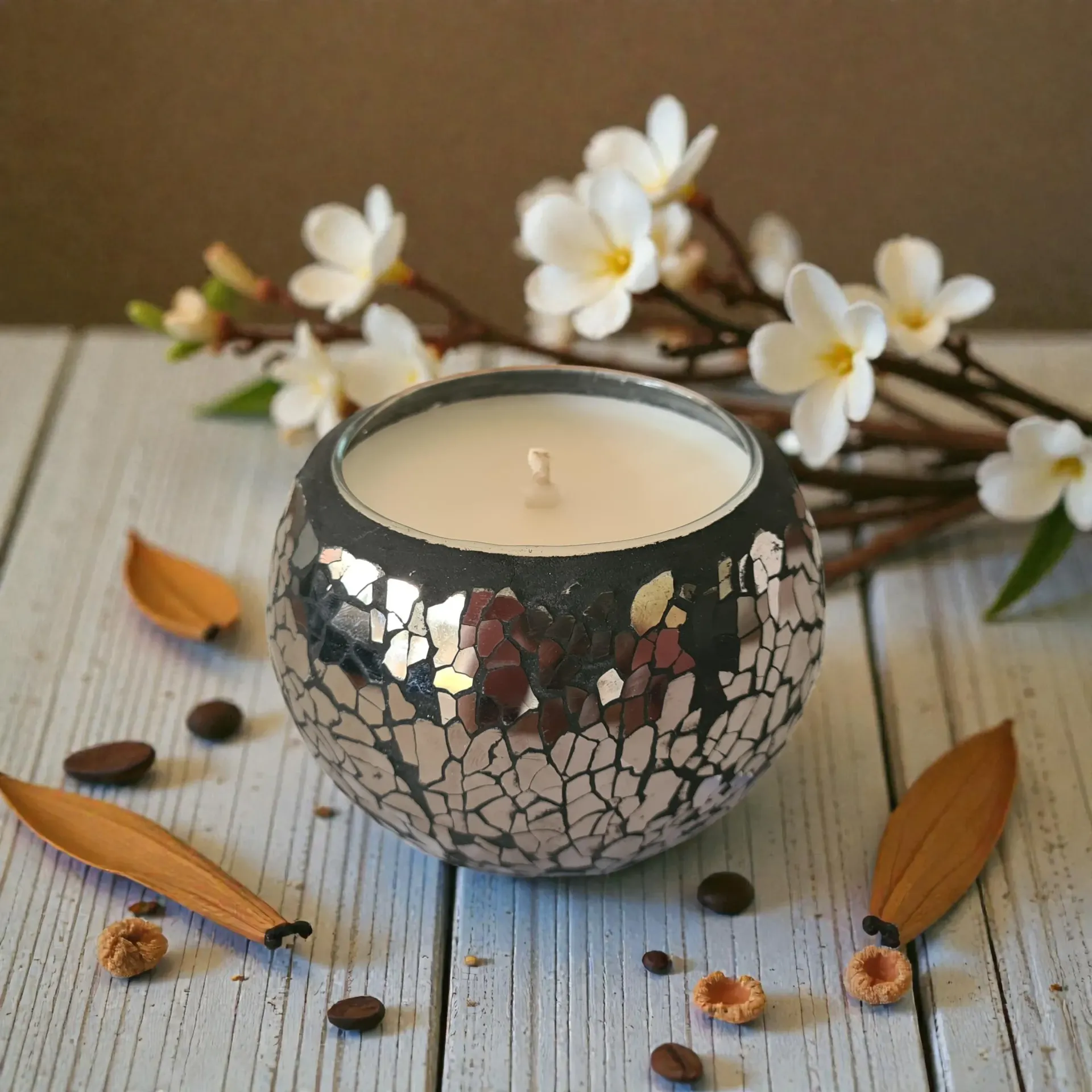 Decorative mosaic candle on a rustic table with white flowers and dried petals around it