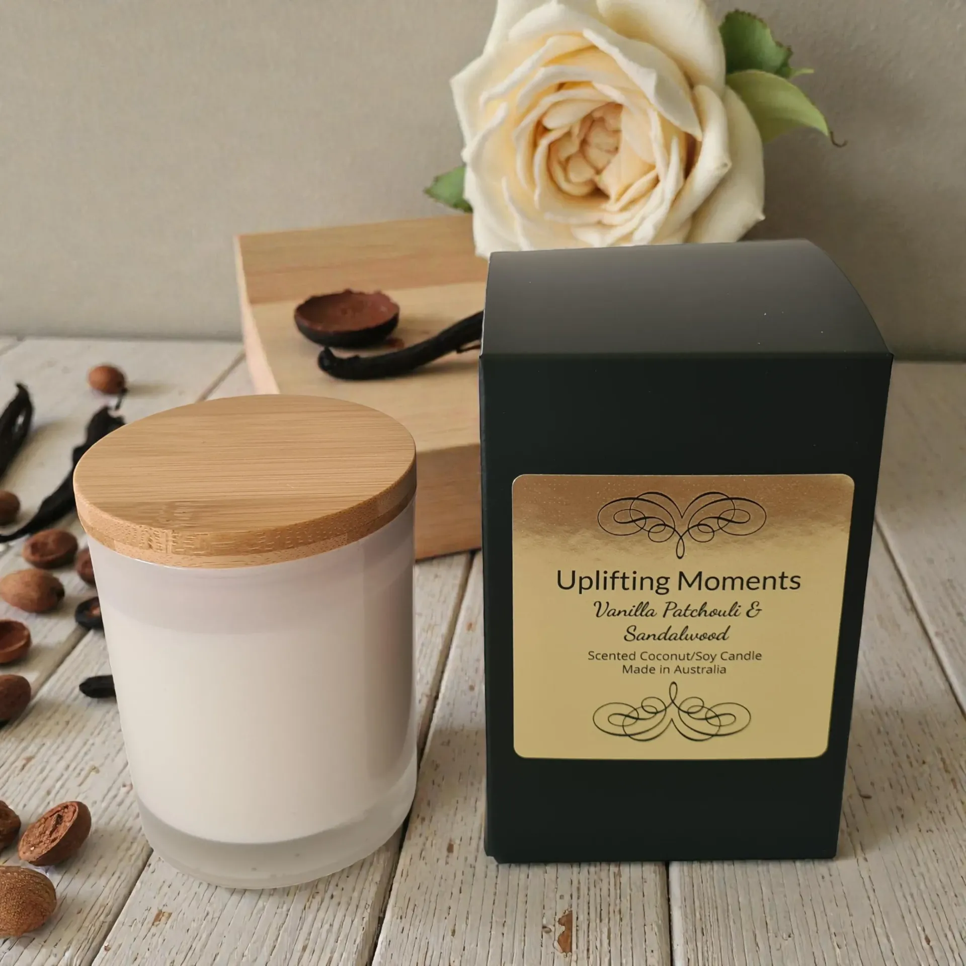 White candle with wooden lid beside black aromatherapy box, scattered coffee beans, and white flowers on a table