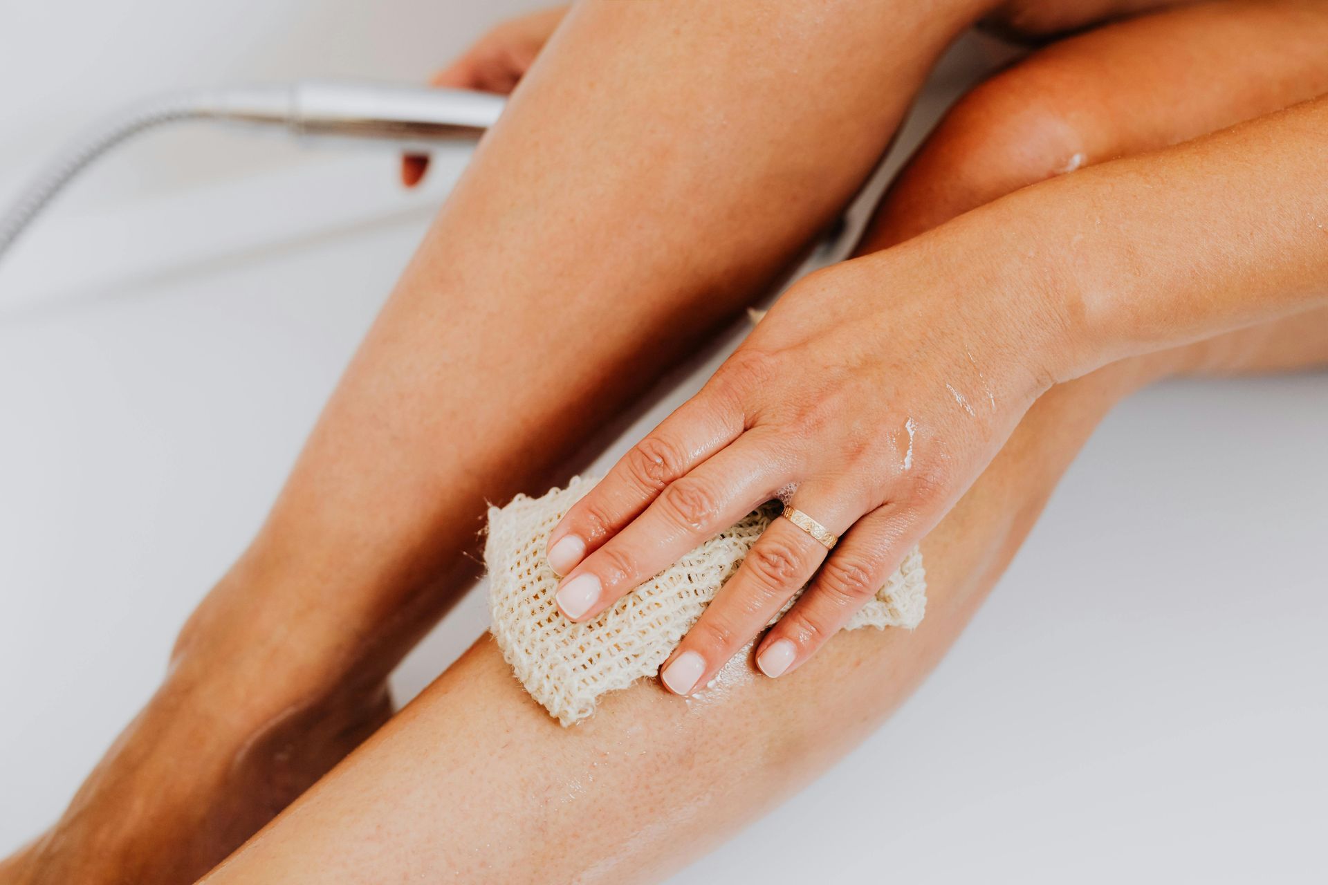 A person gently scrubbing their leg with a textured loofah in a shower.