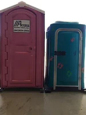 Two portable toilets, one maroon and one blue, standing side by side on a concrete surface