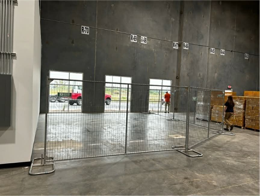 Empty warehouse interior with temporary metal fencing and two workers near stacked materials