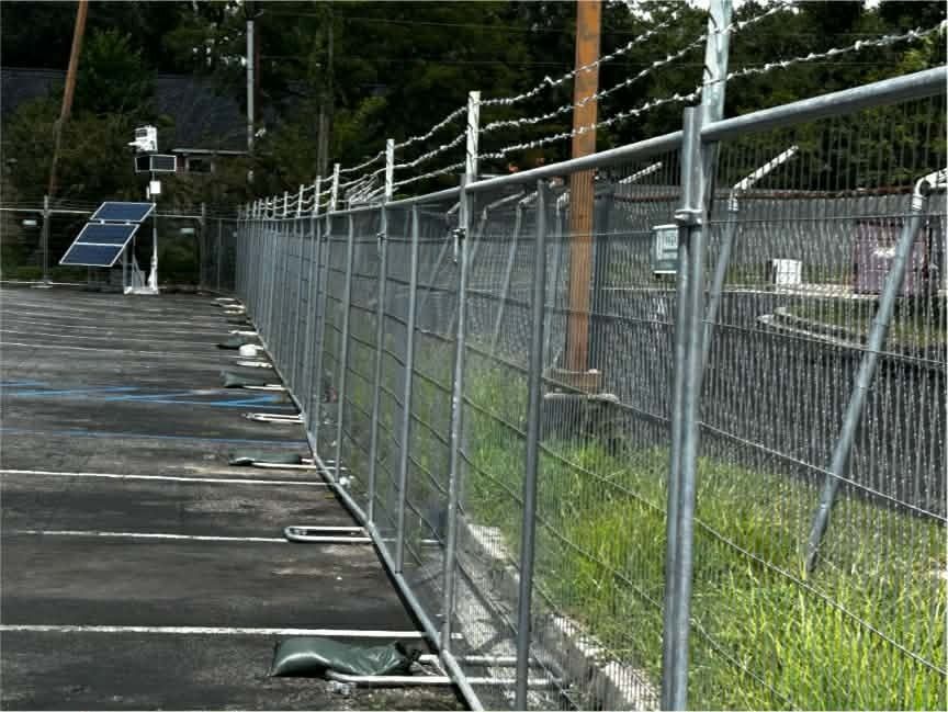 A chain-link fence along a wooden dock beside grassy water, with a solar panel in the background.
