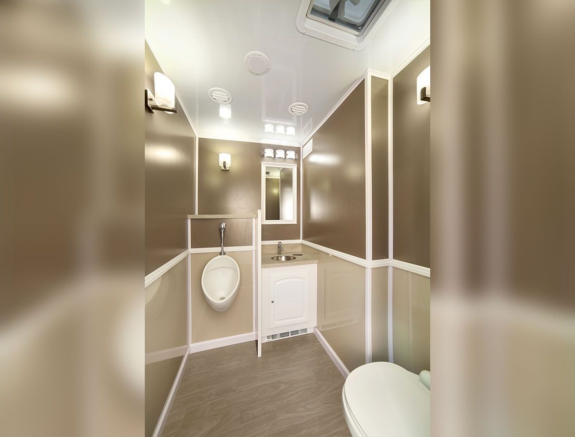 Compact beige bathroom with toilet, sink, wall lights, and mirror