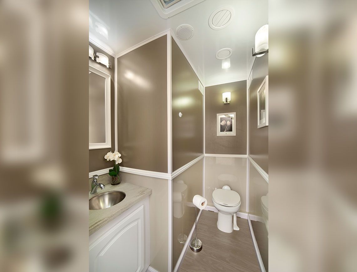 Small beige powder room with a toilet, pedestal sink, mirror, and framed wall art.