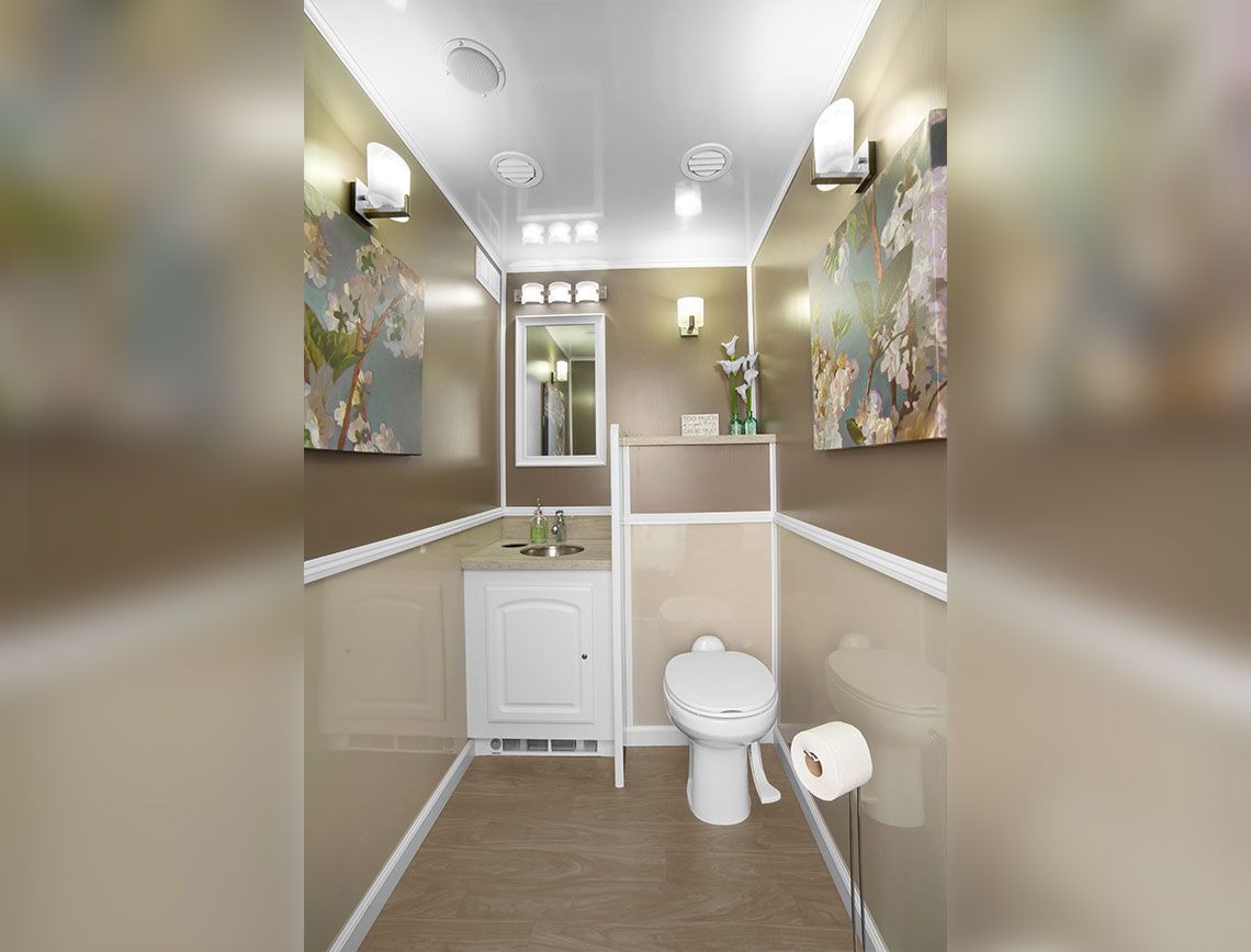 Small beige bathroom with toilet, sink, mirror, and wall art under bright ceiling lights.