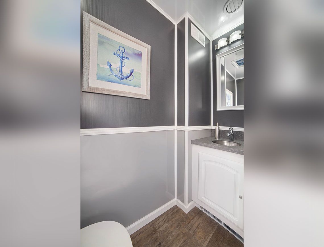Gray-and-white bathroom with anchor wall art, vanity mirror, and wood-look floor tile