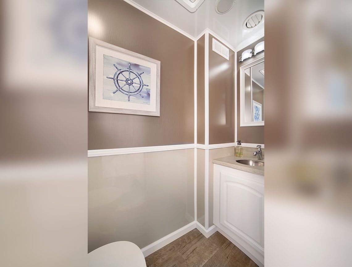 Small bathroom corner with beige walls, white trim, framed nautical art, and a vanity mirror.