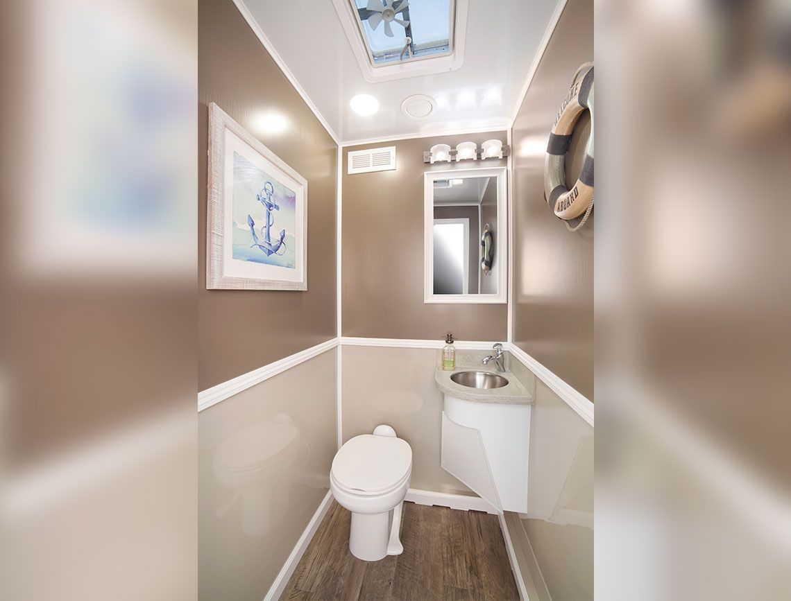 Small beige bathroom with toilet, sink, mirror, and framed wall art.