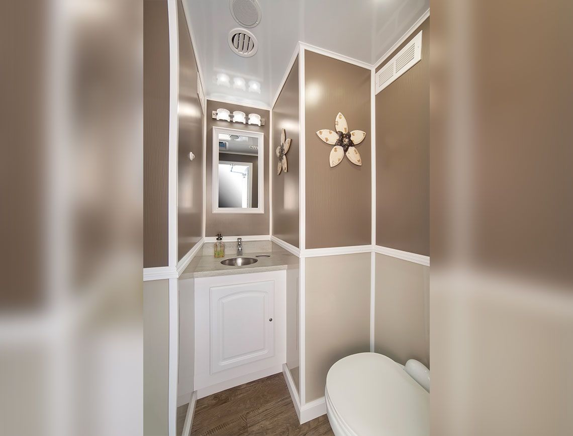Narrow beige bathroom with white trim, vanity, mirror, and toilet under bright ceiling lights