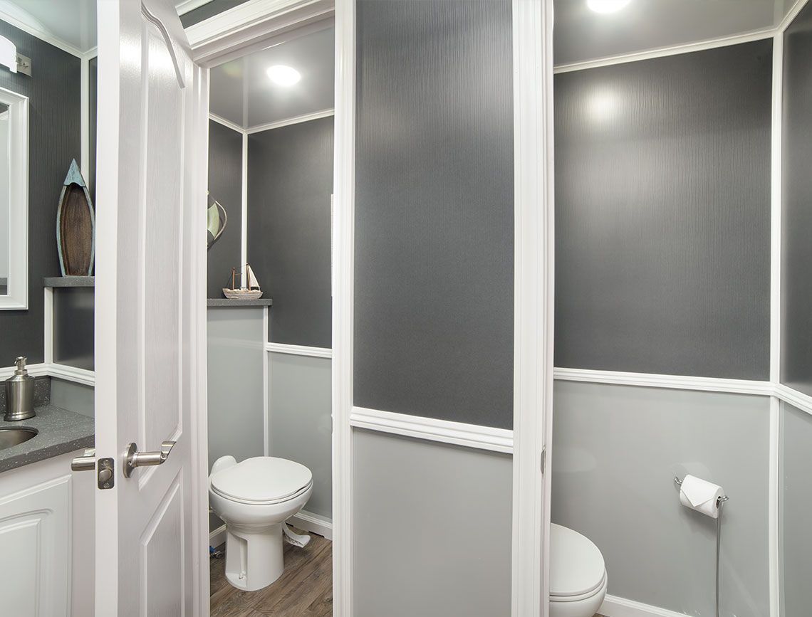 Compact gray-and-white bathroom with toilet, sink, and shower, separated by frosted panels.