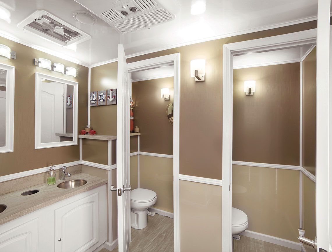 Bright restroom with multiple stalls, beige walls, white trim, sink, mirror, and ceiling lights