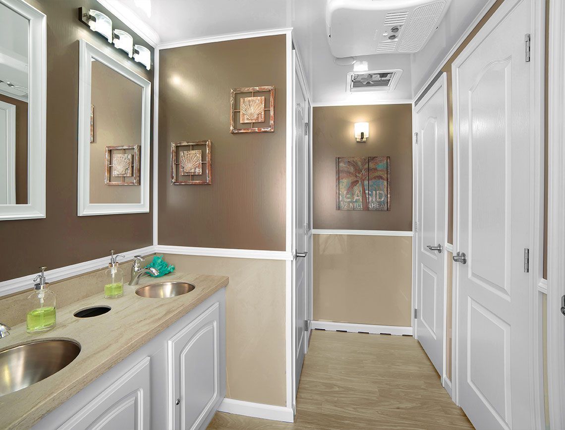 Bright bathroom with double sinks, mirrors, white cabinets, and beige walls leading to a hallway.