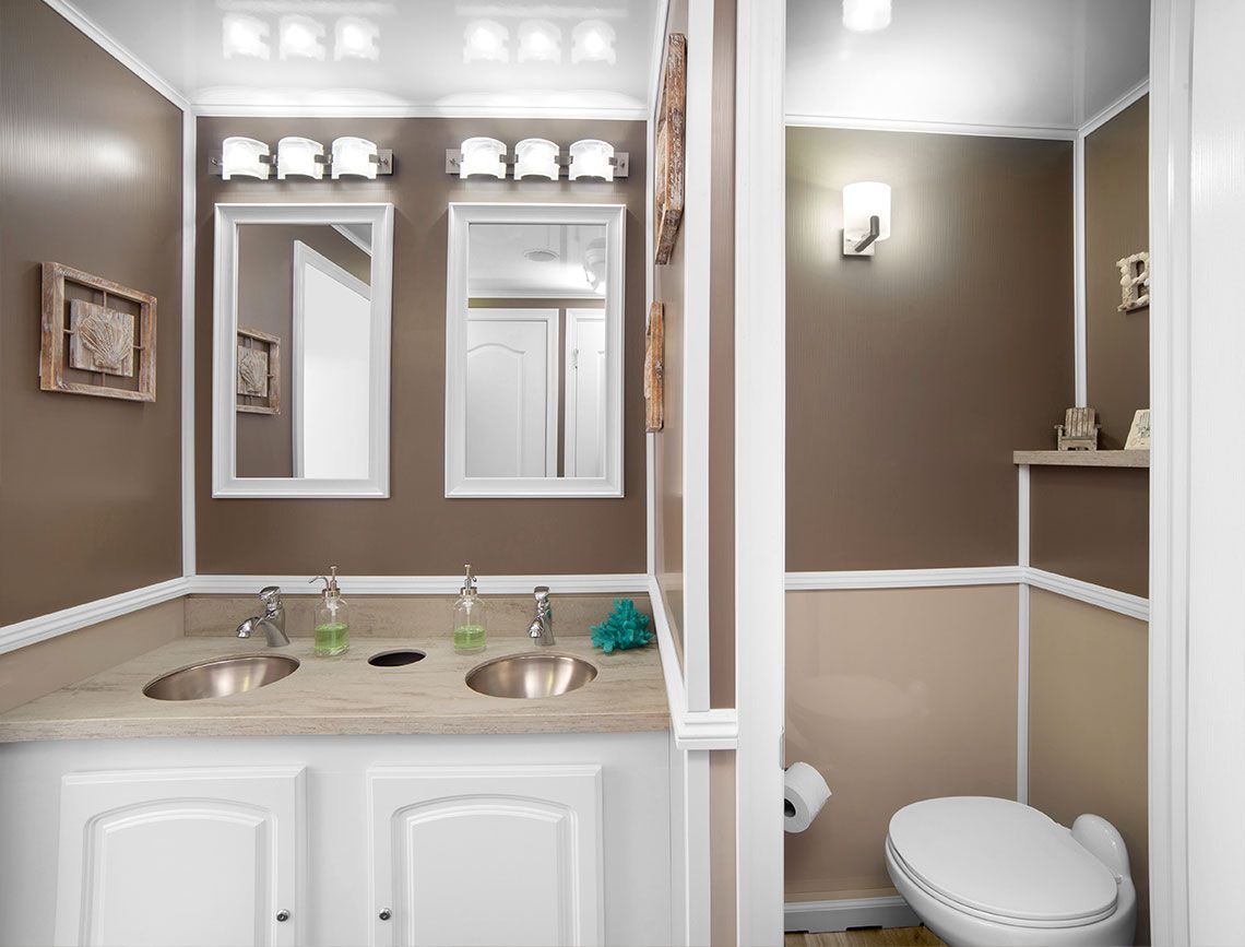 Bathroom vanity with double sinks, mirrors, and a toilet in a beige and white room