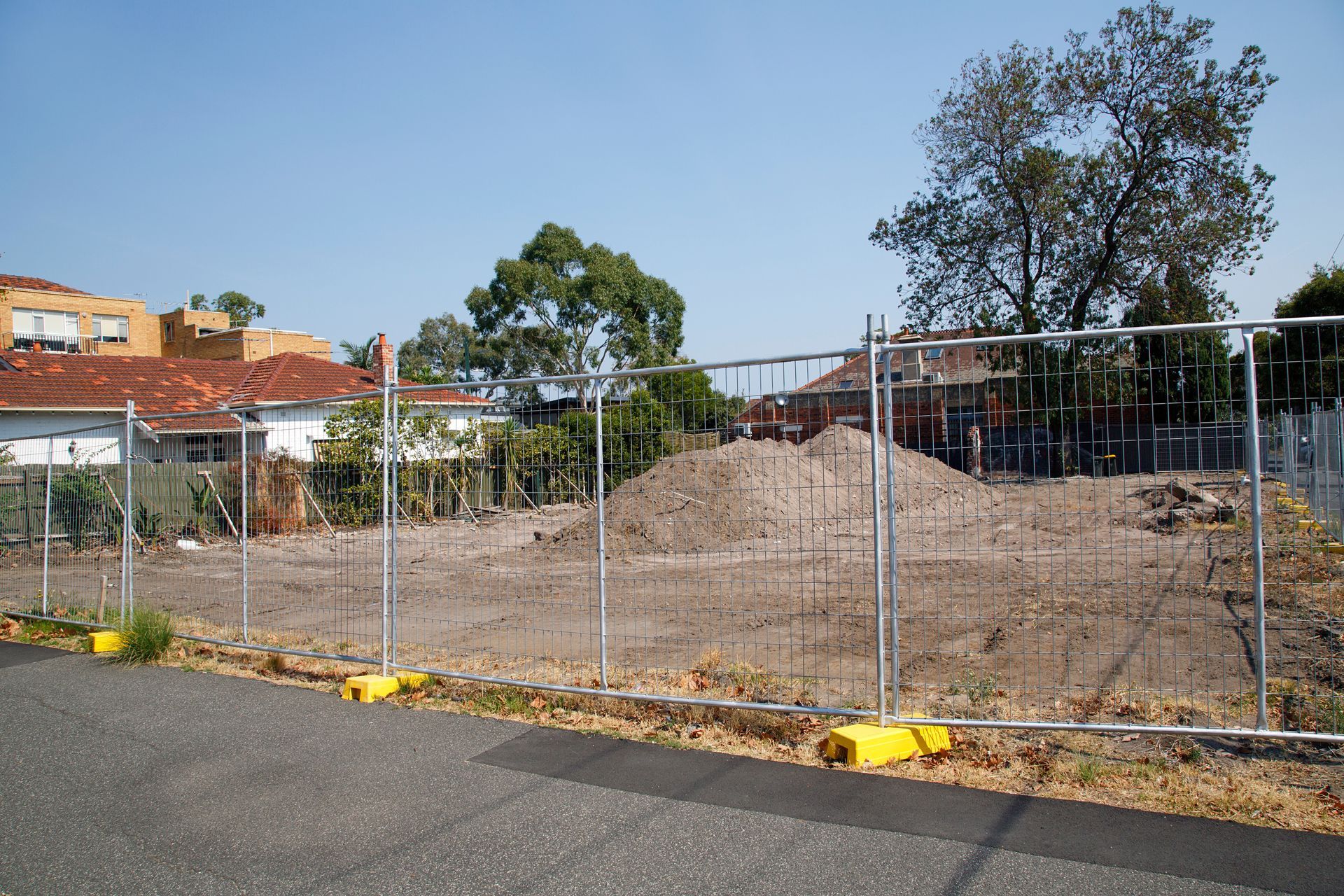 Metal construction fencing encloses a cleared building site beside a suburban street.