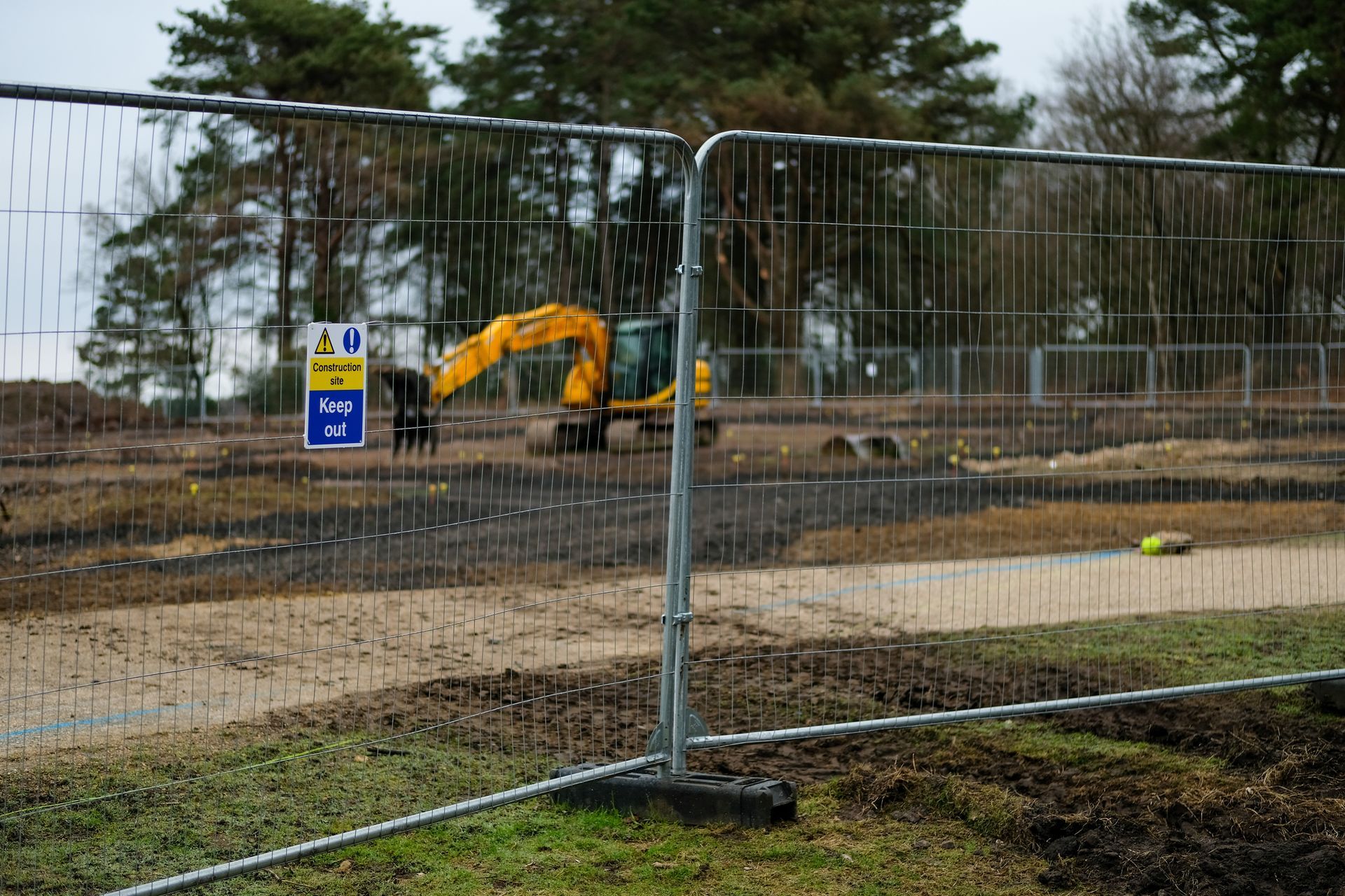 Temporary metal fencing surrounds an active construction site with heavy equipment visible in the background.