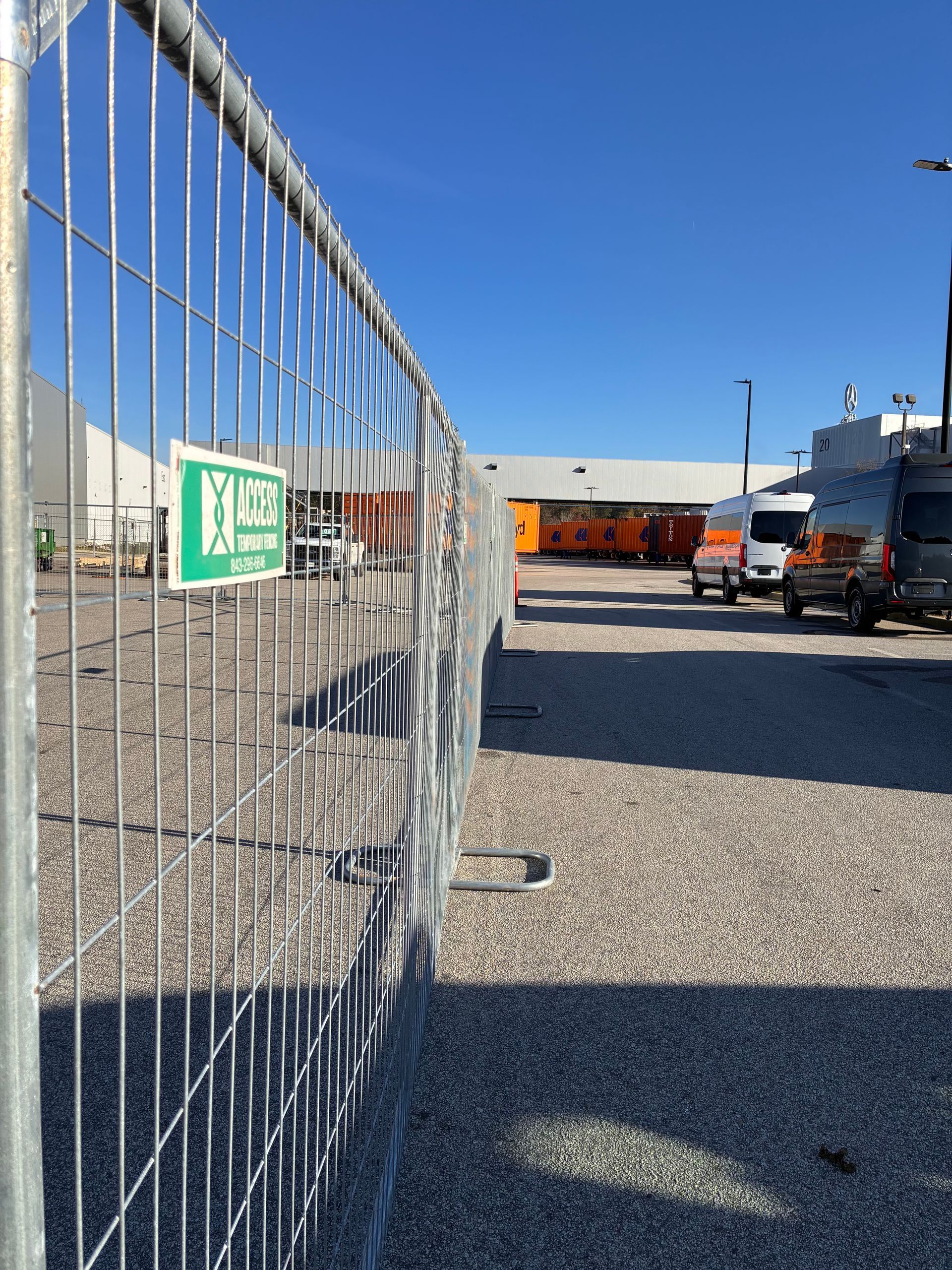 Wire fence beside a gravel lot with orange trucks under a clear blue sky