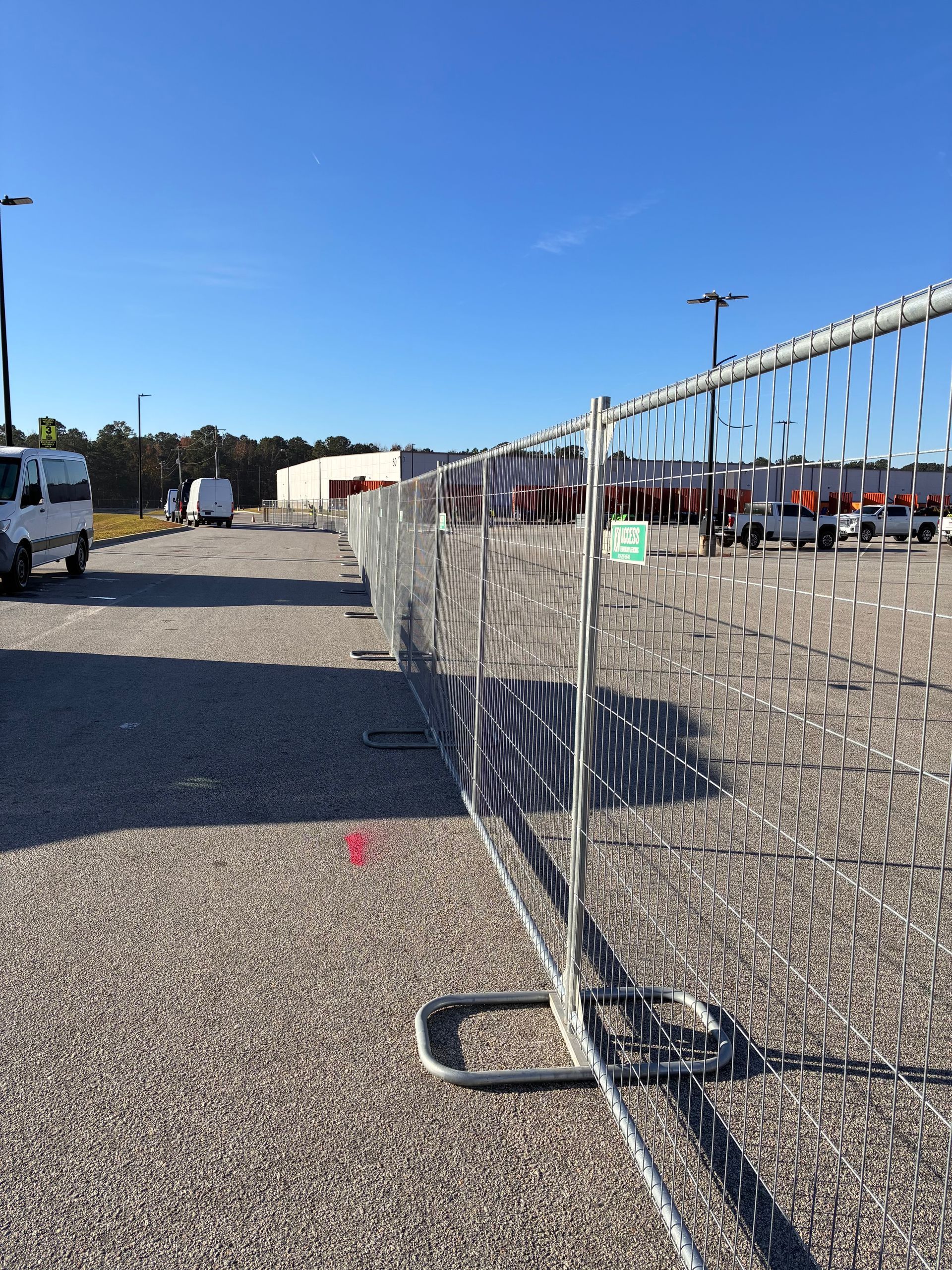 Metal crowd-control fence on gravel at an outdoor event, with tents and vehicles in the background.