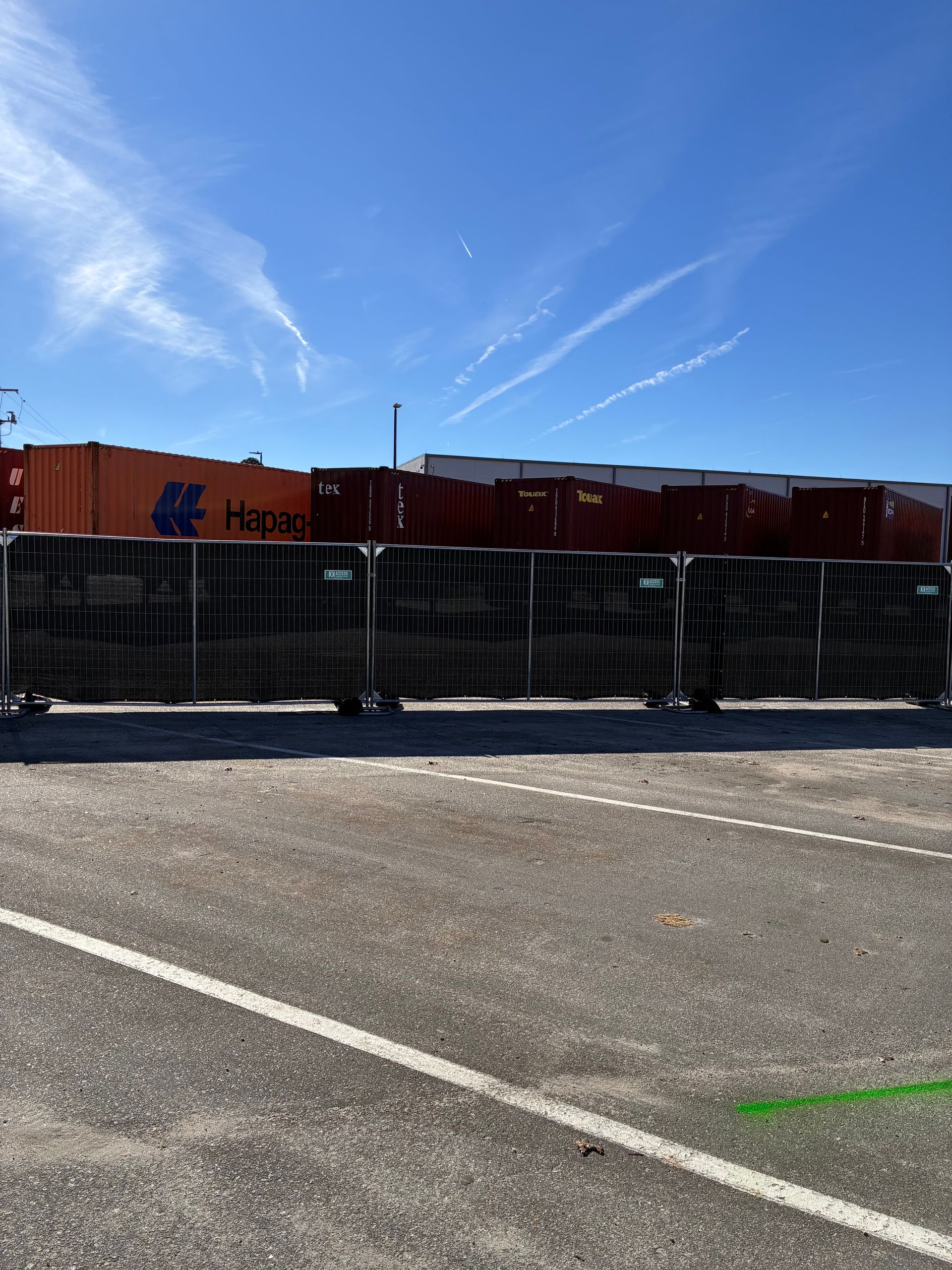 Black metal barricade in front of orange shipping containers under a blue sky at an industrial site