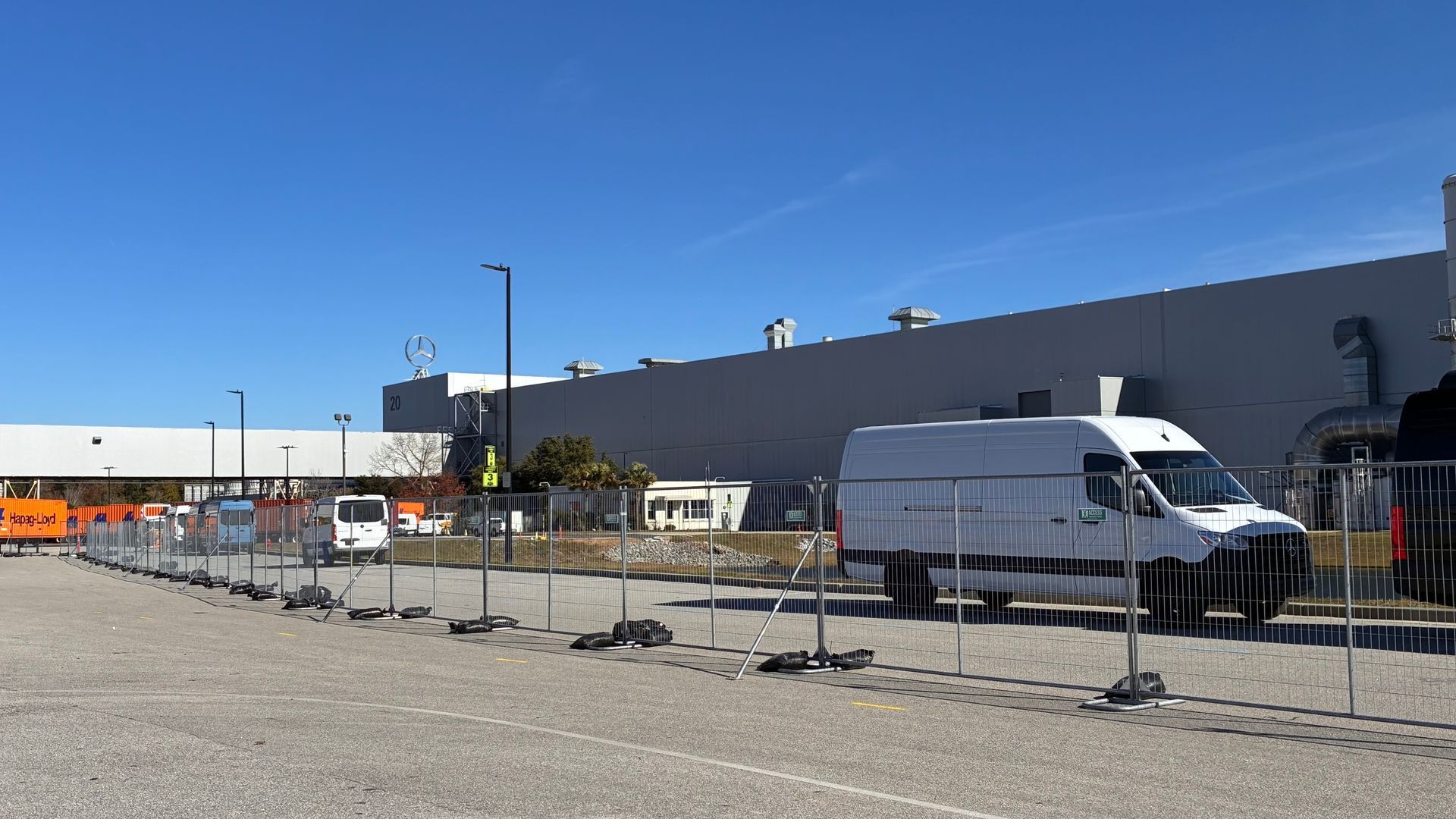 Parking area beside a large gray building with metal barriers, white vans, and a clear blue sky