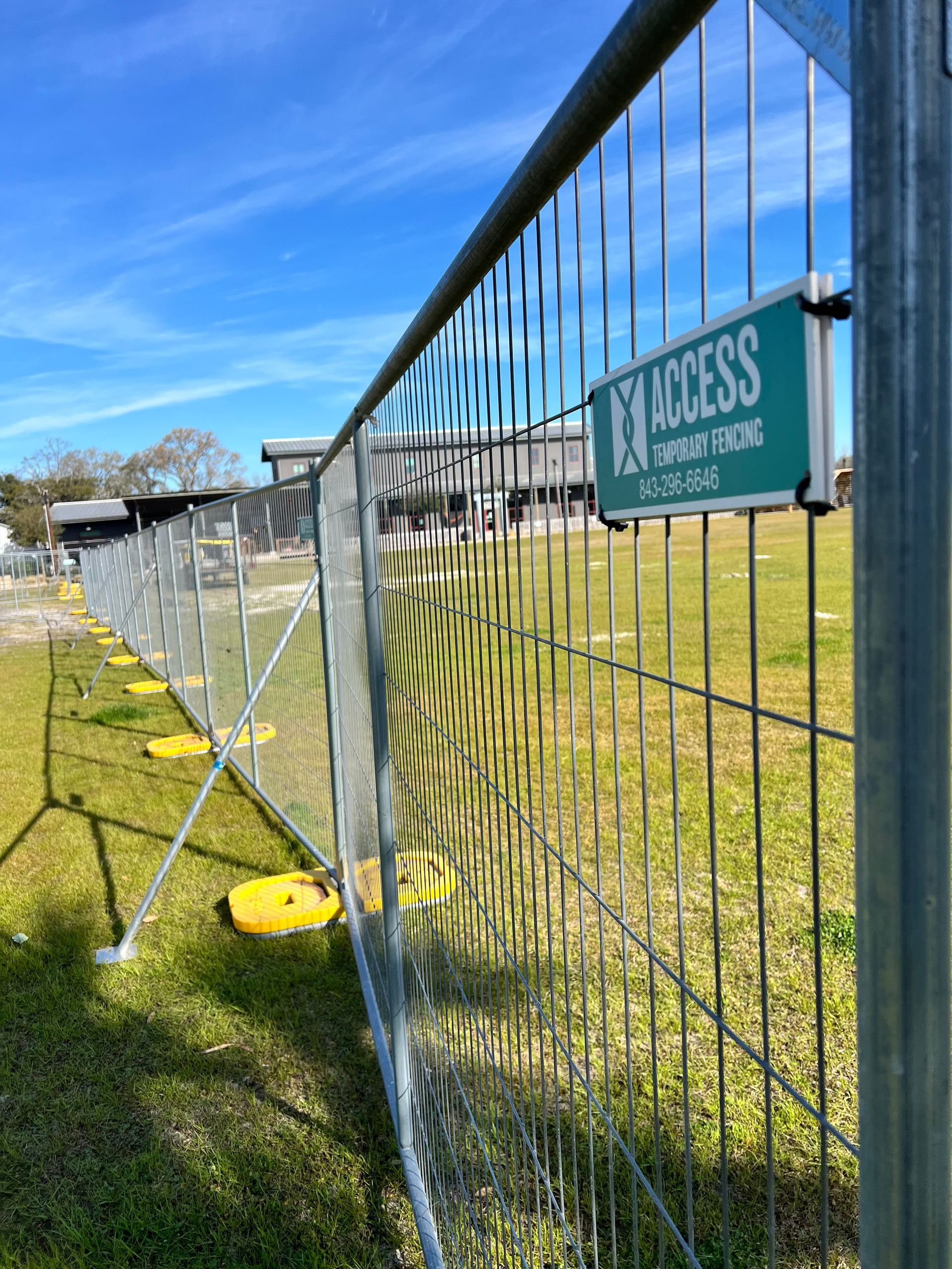 Wire fence with a green “ACCESS” sign beside a grassy field under a blue sky.